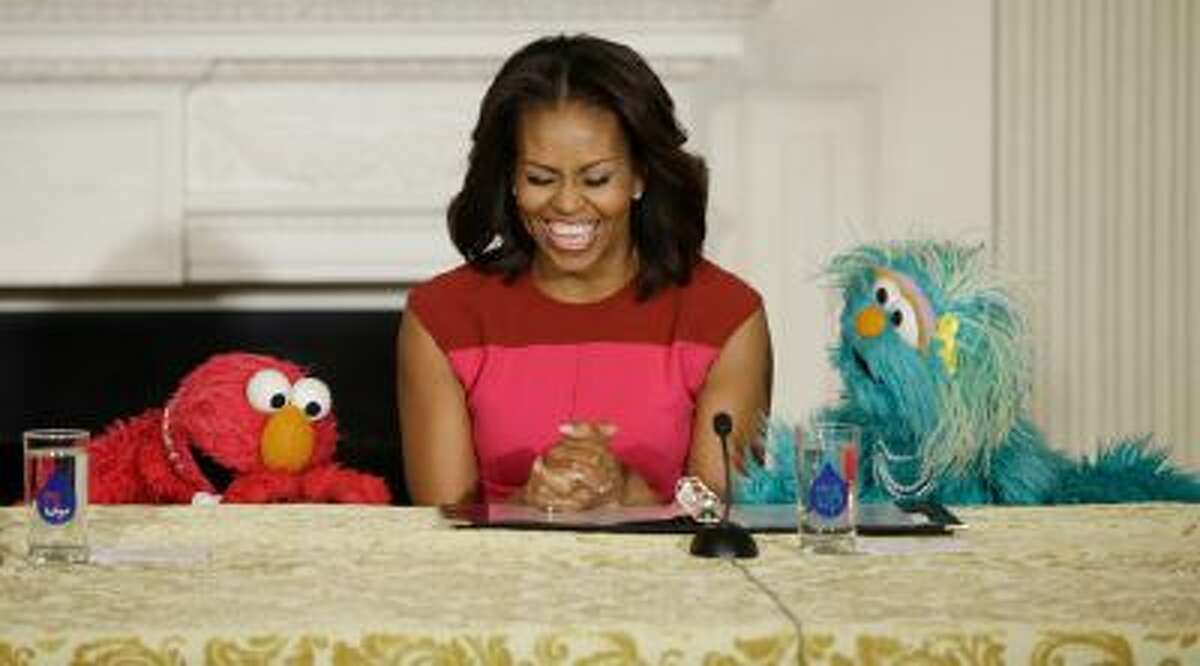 First lady Michelle Obama, center, with PBS Sesame Street's characters Elmo, left, and Rosita, right, as they help promote fresh fruit and vegetable consumption to kids in an event in the State Dining Room of the White House in Washington, Wednesday, Oct. 30, 2013.