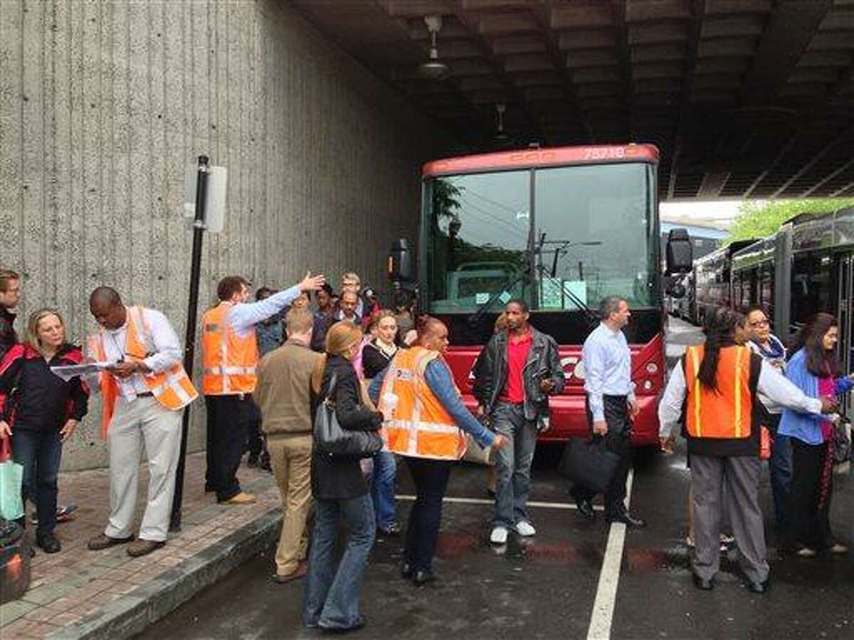 Metro North employees, in orange vests, help transfer westbound commuters at the transportation center in Bridgeport, Ct., to buses Monday, May 20, 2012, after a train collision on Friday injured 72 people and disrupted rail service into New York City. The commuters had arrived from New Haven by train and were being bused to Stamford, Ct., where rail service to New York was available. (AP Photo/Mark Lennihan)