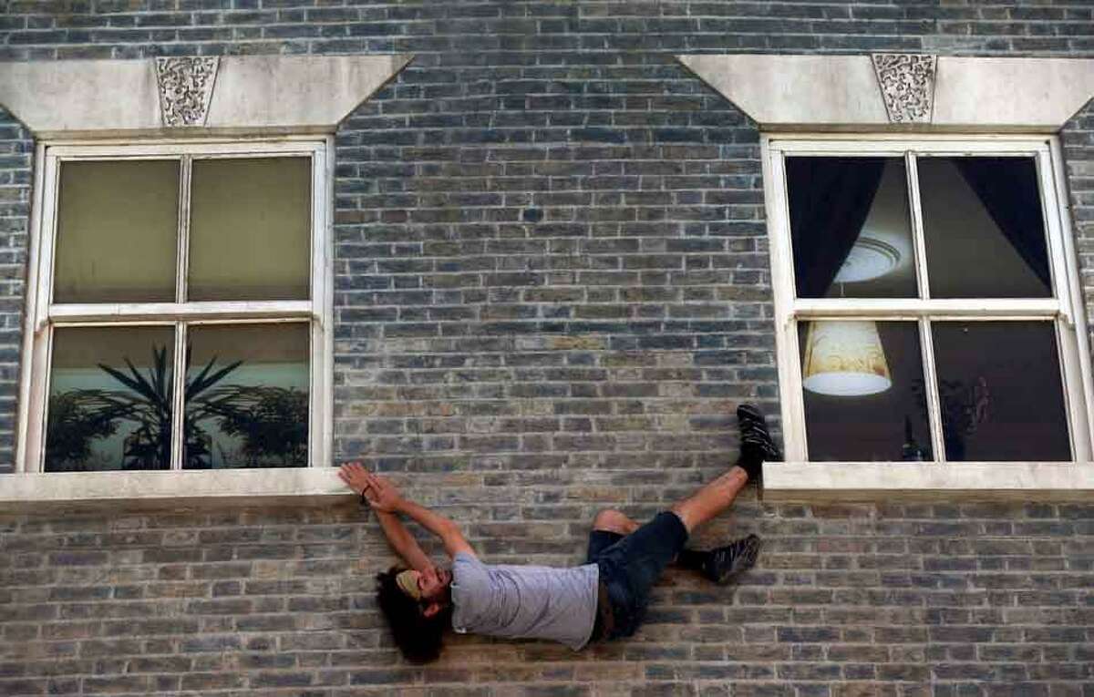 A visitor enjoys an art installation by Argentine artist Leandro Erlich in east London, Tuesday, July 9, 2013. Internationally known for his three-dimensional visual illusions, Erlich has been commissioned to create a new installation in Dalston area of the capital. Resembling a theatre set, the detailed facade of a Victorian terraced house, recalling those that once stood on the street, lies horizontally on the ground with mirrors positioned overhead. The reflections of visitors give the impression they are standing on, suspended from, or scaling the building. (AP Photo/Lefteris Pitarakis)