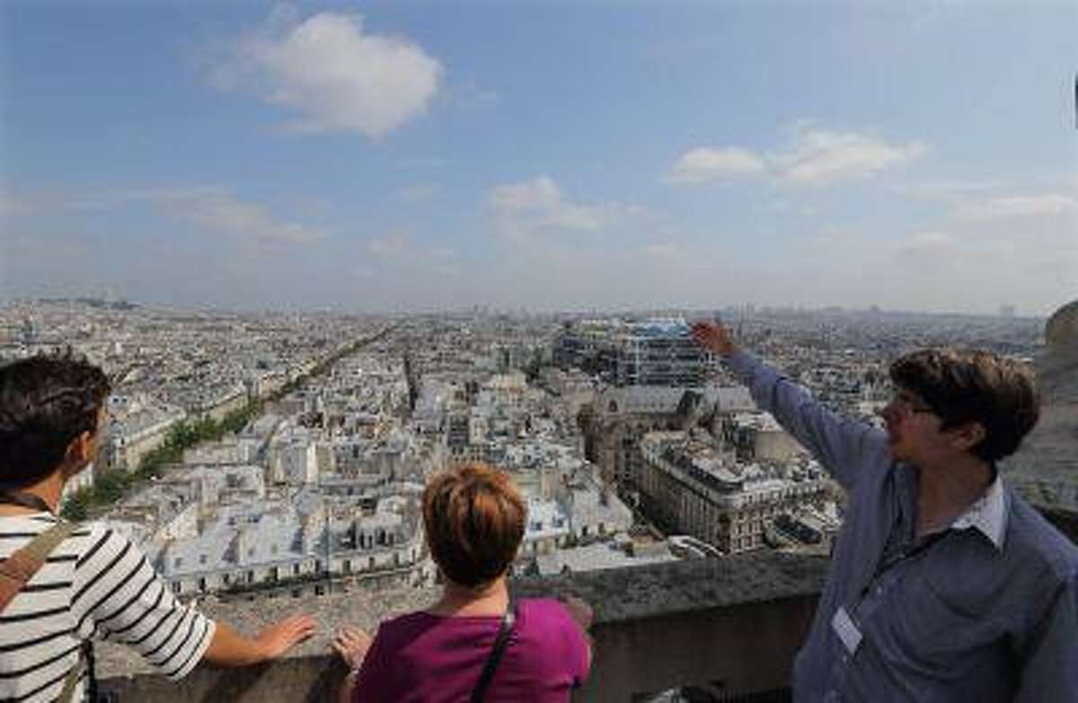 Tour guide David (R) gives explanations to visitors as they look at the Paris skyline from the zinc-topped terrace of the Tour Saint-Jacques in Paris July 5, 2013. It's not for the short of breath or those weak in the knees, but the dizzying 360-degree vista of Paris from the Tour Saint-Jacques is one of the best-kept secrets of the French capital. For one good reason: this flamboyant 16th-century Gothic tower, a famous passing point for pilgrims headed to Santiago de Compostela in Spain, had been closed to the public for most of its 500-year history.Now open to tourists until September 15, the 62-metre (203 foot) tower offers stunning bird's eye views - provided you have the energy to walk up its claustrophobic 300-step spiral staircase. REUTERS/Philippe Wojazer (FRANCE - Tags: SOCIETY TRAVEL)
