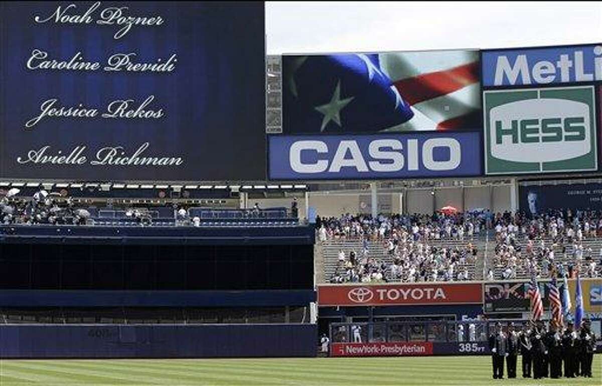 An honor guard of Newtown, Connecticut first responders stands at attention as names of the victims of the Newtown school massacre are shown on a huge video screen in a pregame ceremony prior to the Baltimore Orioles baseball game against the New York Yankees, Sunday, July 7, 2013, at Yankee Stadium in New York. (AP Photo/Kathy Willens)