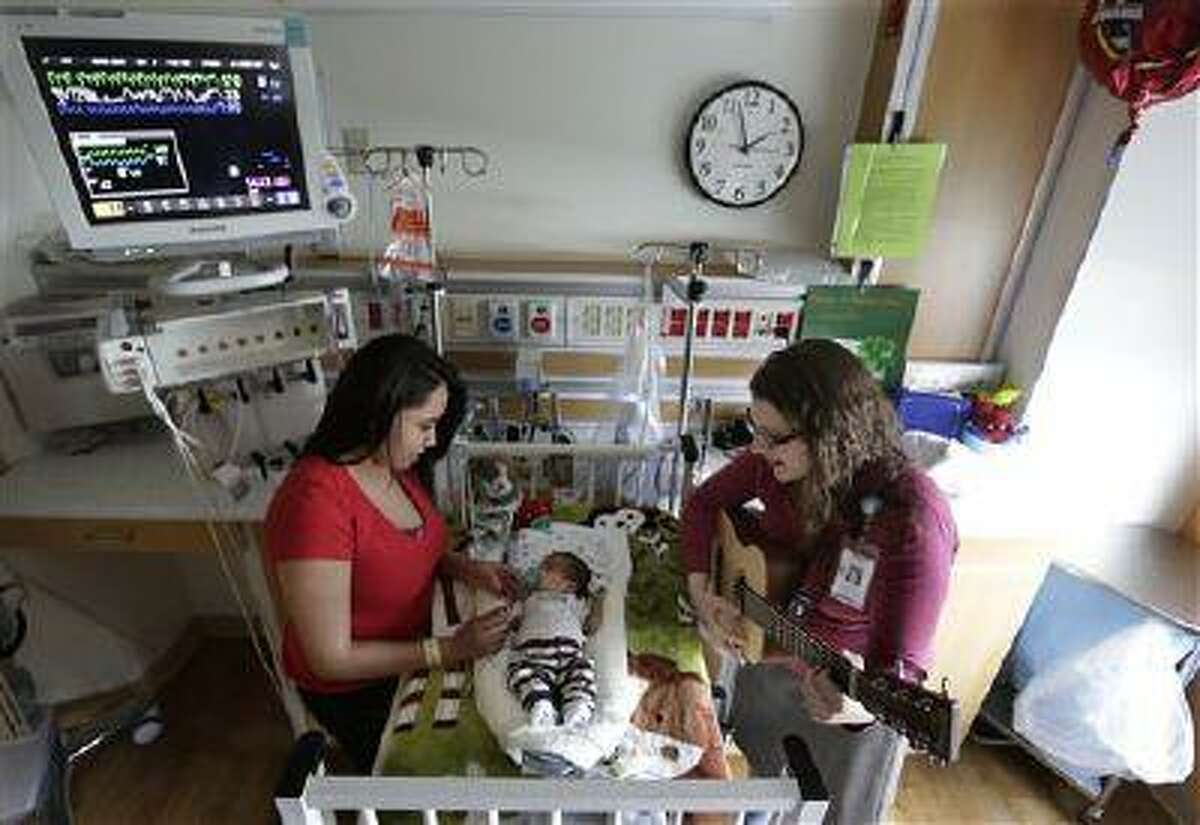 Music therapist Elizabeth Klinger, right, quietly plays guitar and sings for Augustin as he grips the hand of his mother, Lucy Morales, in the newborn intensive care unit at Ann & Robert H. Lurie Children's Hospital in Chicago on Monday, May 6, 2013. "The music relaxes him, it makes him feel more calm" and helps him sleep better too, Lucy Morales said. "Sometimes it makes us cry."