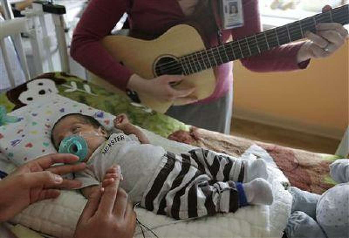 Music therapist Elizabeth Klinger, right, quietly plays guitar and sings for Augustin as he grips the hand of his mother, Lucy Morales, in the newborn intensive care unit at Ann & Robert H. Lurie Children's Hospital in Chicago on Monday, May 6, 2013. Research suggests that music may help those born way too soon adapt to life outside the womb. Recent studies and anecdotal reports suggest the vibrations and soothing rhythms of music, especially performed live in the hospital, might benefit preemies and other sick babies.