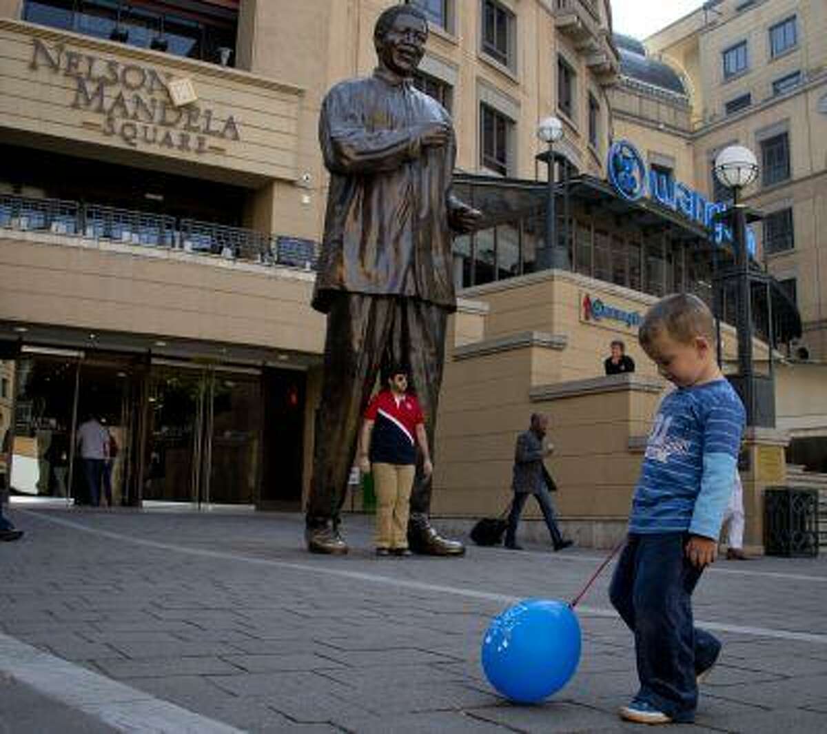 A young boy plays with a balloon in front of a giant bronze statue of Nelson Mandela at Nelson Mandela square in the north Johannesburg suburb of Sandton on June 28, 2013.