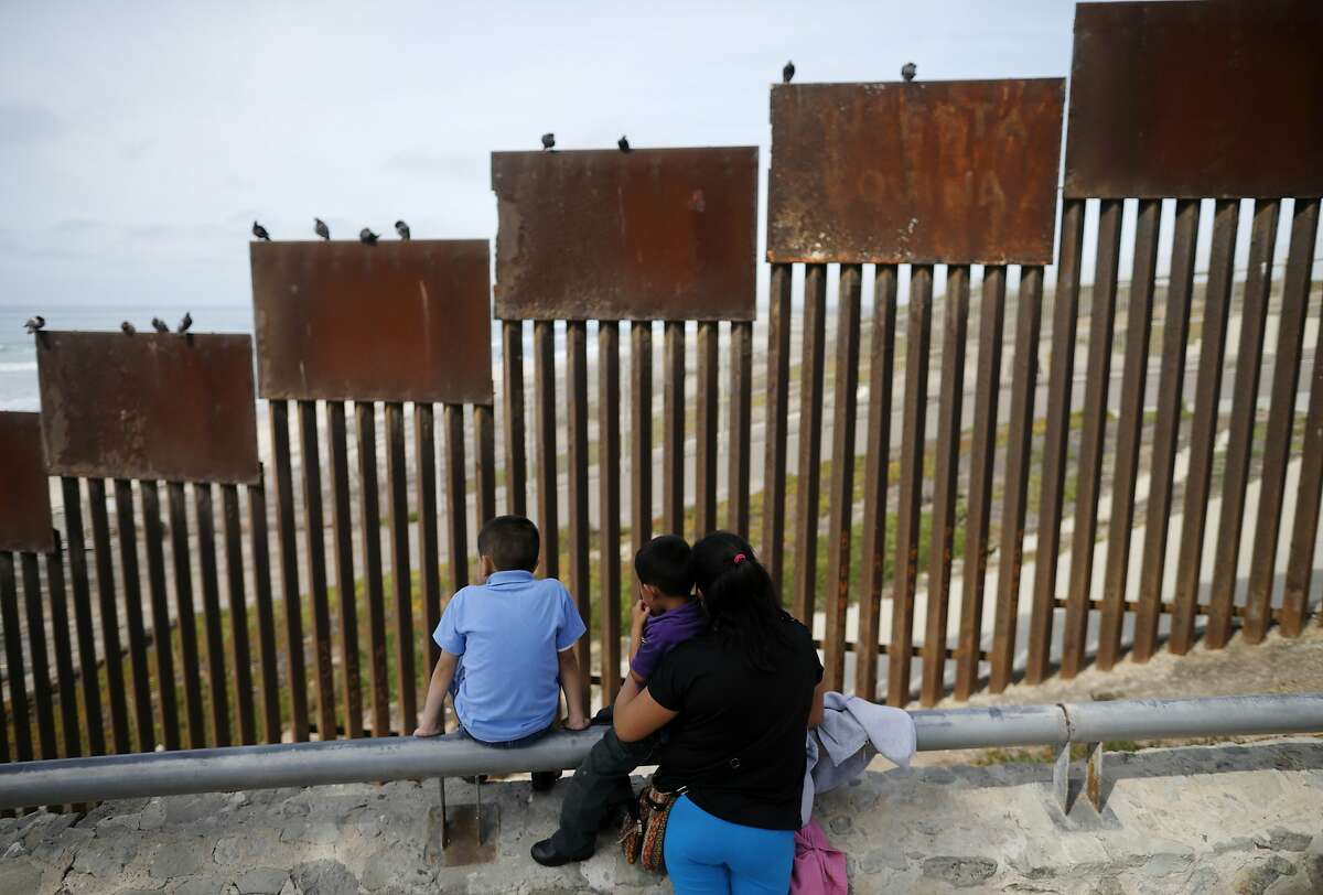 FILE - In this March 2, 2016 file photo, a family looks towards metal bars marking the U.S. border where it meets the Pacific Ocean, in Tijuana, Mexico. Candidate Donald Trump's promise to build a "big, beautiful wall" on the Mexican border conjured images of an inpenetrable structure spanning 2,000 miles. Trump still insists he'll build the wall, but his top aides have made clear it won't be "from sea to shining sea." (AP Photo/Gregory Bull, File)