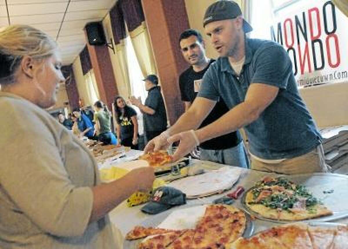 Catherine Avalone/The Middletown Press Manager of Mondo's Pizza Keith Vibert, at right and head chef Dave Noad serves up a slice of their winning pizza to Jessica Rose, of Northford at the Second Annual Middletown Pizza War held at the Sons of Italy on Court Street in Middletown Wednesday evening. Carmine's of Durham placed second and DaVinci Pizza placed third. The event is sponsored by Feed the People Charity and proceeds will benefit St. Vincent dePaul Middletown.