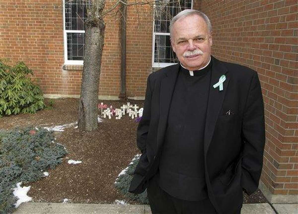 Monsignor Robert Weiss, who officiated at the funerals of eight children following the massacre at the Sandy Hook Elementary School, stands in front of a makeshift memorial at St. Rose of Lima Roman Catholic Church in Newtown, Conn. Rev. Weiss says he?s seen estranged families reconciling, strangers hugging on the street and neighbors meeting neighbors for the first time. AP Photo/Pat Eaton-Robb