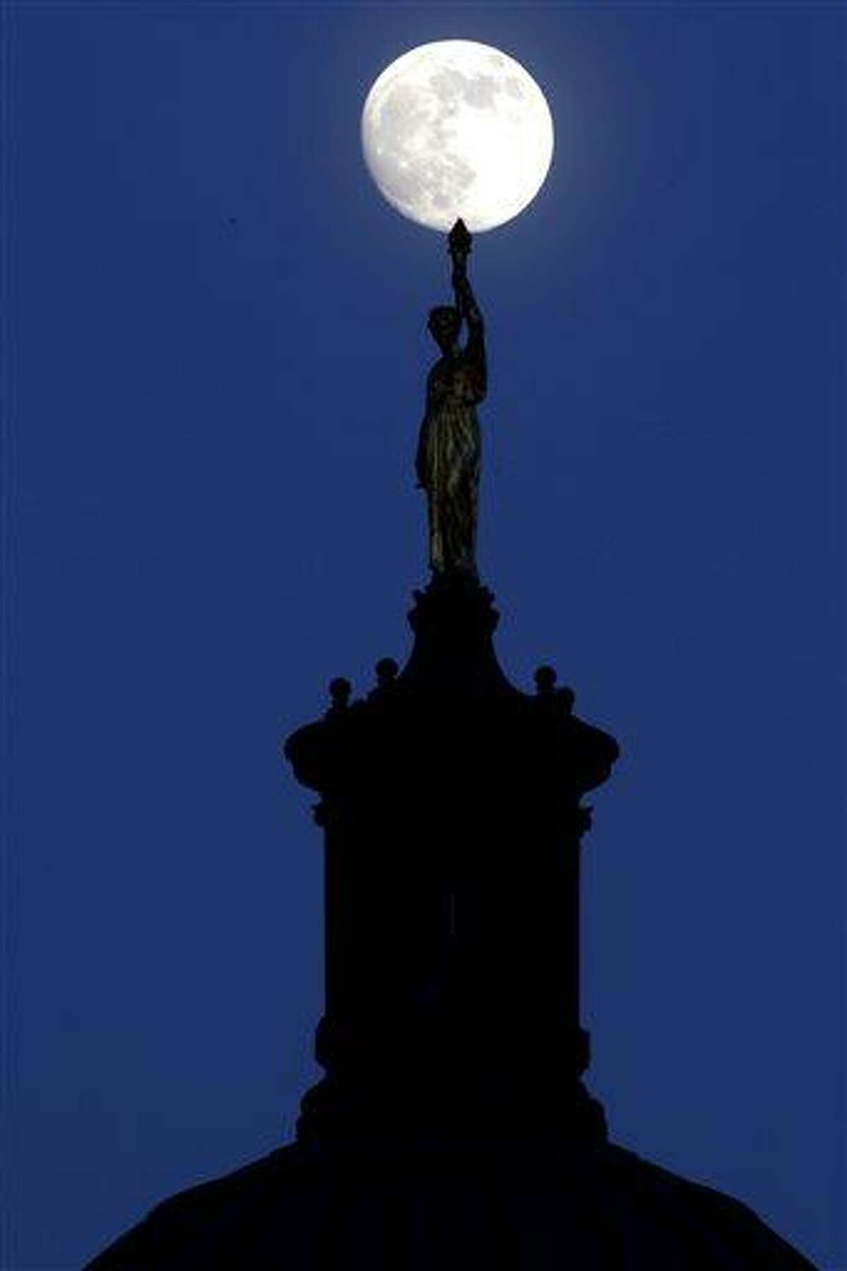 The moon in its waxing gibbous stage shines over a statue entitled "Enlightenment Giving Power" by John Gelert, which sits at the top of the dome of the Bergen County Courthouse in Hackensack, N.J., Friday, June 21, 2013. The moon, which will reach its full stage on Sunday, is expected to be 13.5 percent closer to earth during a phenomenon known as supermoon. (AP Photo/Julio Cortez)