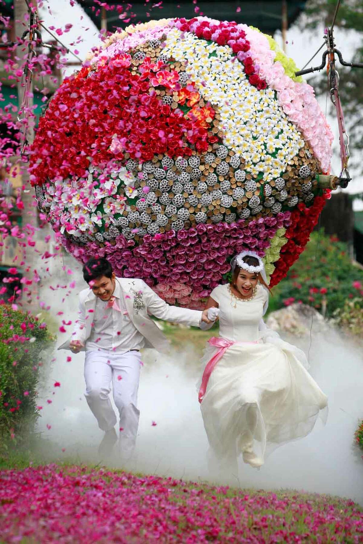 Prasit Rangsitwong, left, and Varutton Rangsitwong run away from a giant flower ball as a part of an adventure-themed wedding ceremony in Prachinburi province, Thailand, Wednesday, Feb. 13, 2013, on the eve of Valentine's Day. (AP Photo/Wason Wanichakorn)