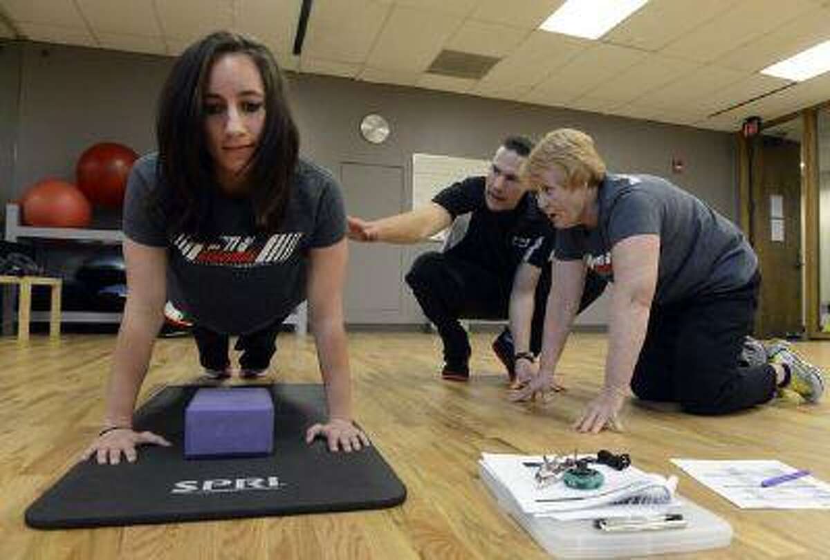 Deena Christy, 61, (right) of Letts, Iowa, works with National Personal Training Institute of Colorado instructor Shawn Agnew (center) on analyzing fellow student Ashli Bradley during a push-up test at the institute in Lakewood. Both Christy and Bradley are learning to become personal trainers.