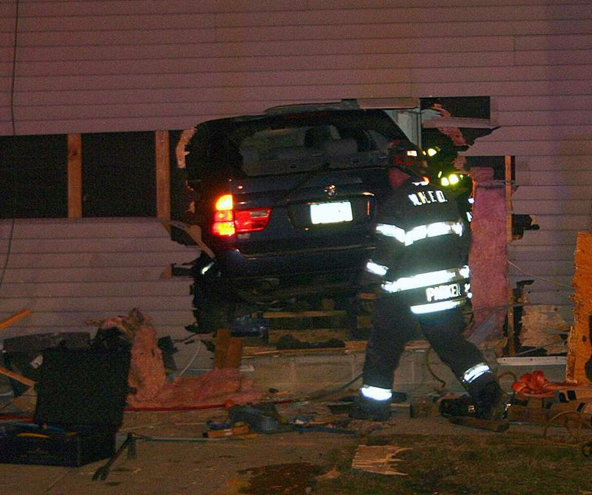 New Haven firefighters work frantically to free a man who was trapped under an SUV as he was sleeping in his bedroom. The vehicle crashed through the house at the corner of Winchester Avenue and Compton Street as it was being chased by police. The driver of the vehicle fled the scene and was still being sought by police. (William Kaempffer/New Haven Register)