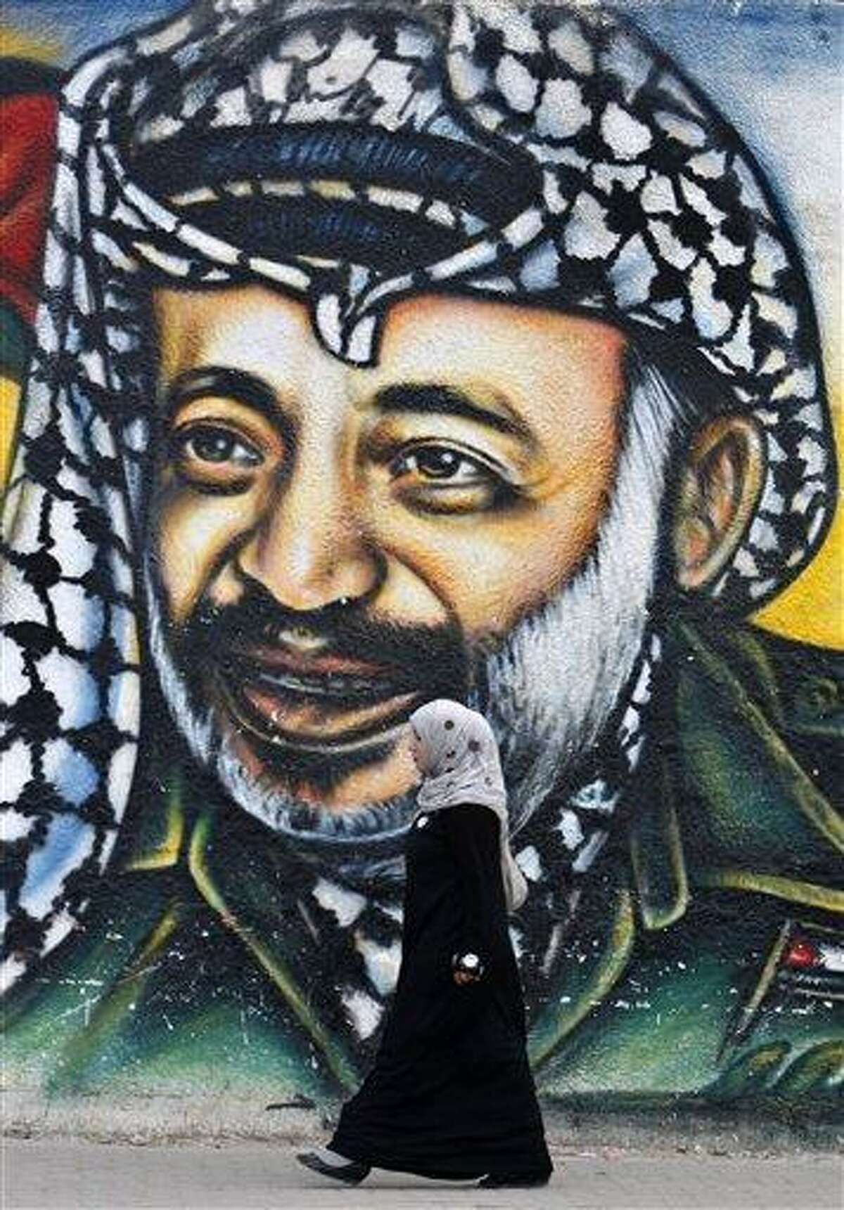A Palestinian woman walks past a mural of late Palestinian leader Yasser Arafat, in Gaza City, Tuesday, Nov. 27, 2012. Palestinian authorities on Tuesday opened Yasser Arafat's grave and foreign experts took samples from his remains as part of a long-shot attempt, eight years after the iconic leader's mysterious death, to determine whether he was poisoned, as relatives and some political successors have claimed. (AP Photo/Adel Hana)