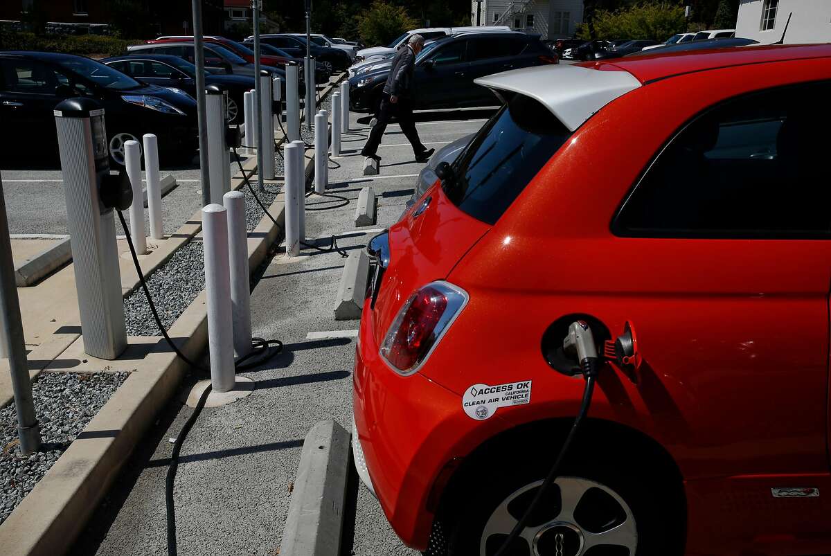 A person walks past electric car charging stations in a parking lot in the Presidio July 25, 2017 in San Francisco, Calif.