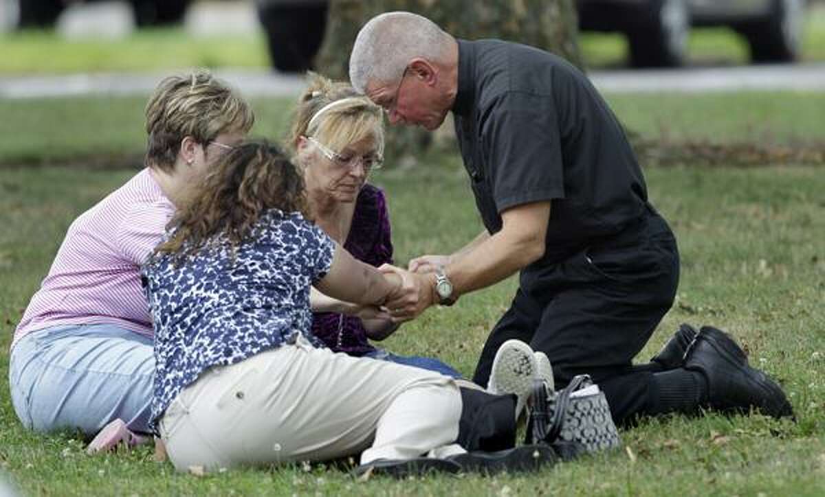 A priest kneels in prayer with three women outside Manchester High School, a gathering point for the families, co-workers and friends of shooting victims in Manchester, Conn., Tuesday, Aug. 3, 2010. A warehouse driver who was asked to resign his job at a beer distributor refused, then opened fire Tuesday morning, a company executive said. Police said the gunman and several other people were killed and others were wounded. (AP Photo/Charles Krupa)