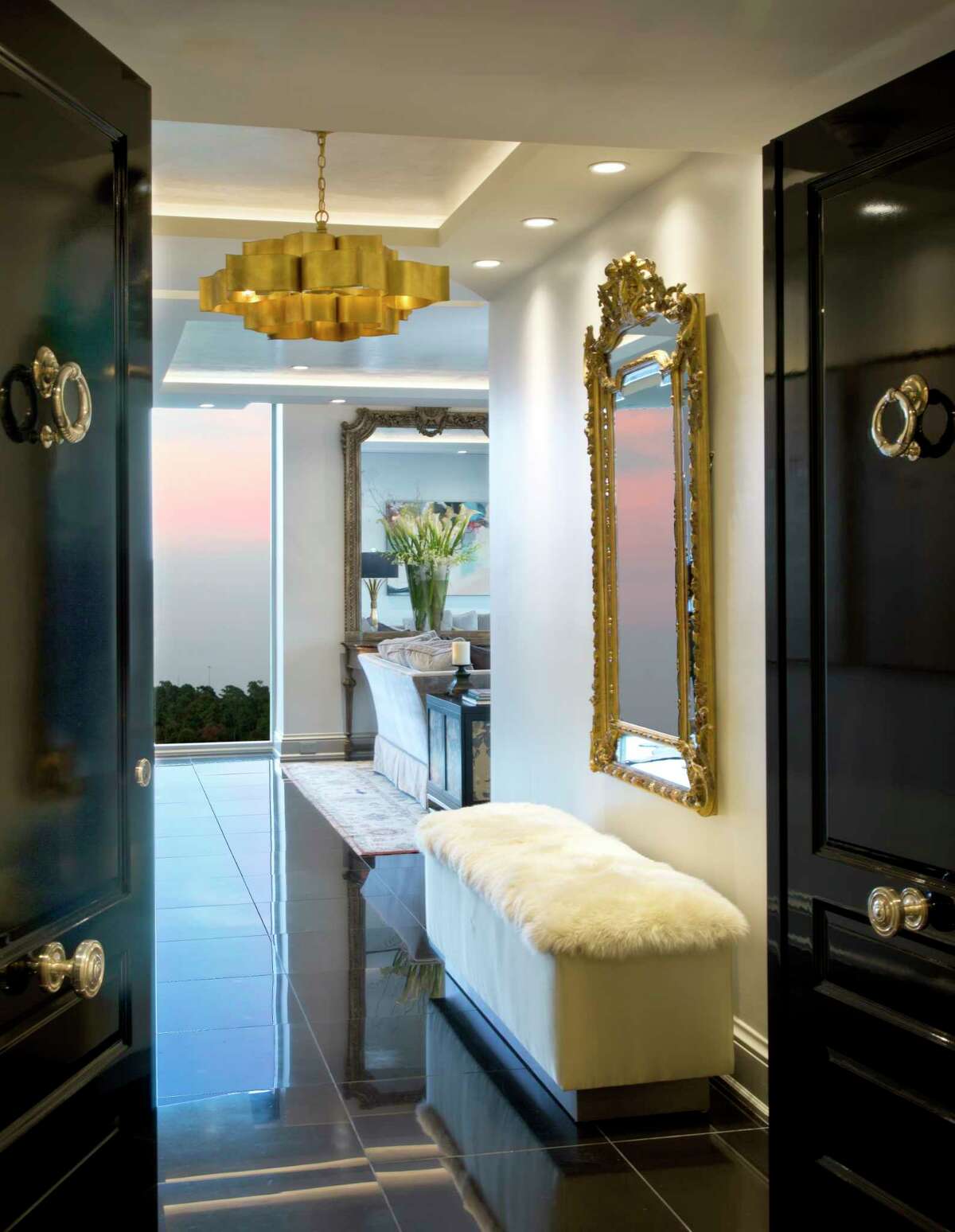 Glossy black doors open to a sophisticated foyer with a contemporary chandelier and sheepskin fur bench.