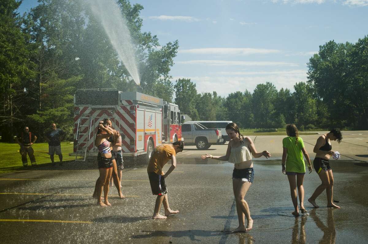 Volunteers taking part in the Call to the Creek group work project, which brings hundreds of high school and college students from around the country to do volunteer work in the Midland area, cool off with help from the Homer Township fire department on Thursday, July 27, 2017 afternoon at Bullock Creek High School, where the students are staying during the group work camp.