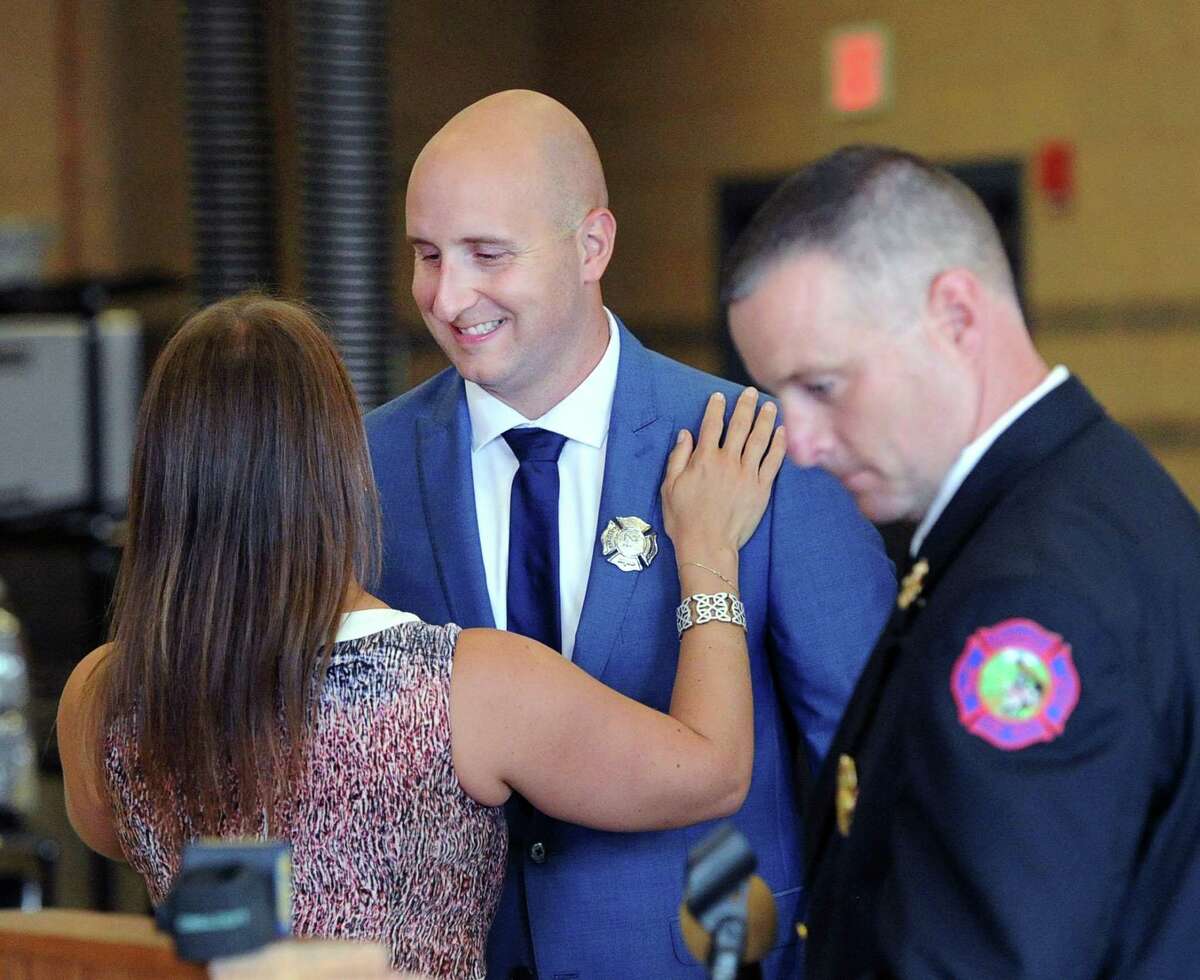 Newly sworn-in Greenwich Firefighter Peter Purcell, center, smiles after his wife Loriane, left, pinned his firefighter's badge on his jacket during the swearing in ceremony for five new Greenwich Firefighters, including Purcell, at Fire Department Headquarters in Greenwich, Conn., Friday morning, July 28, 2017. At right is Assistant Greenwich Fire Chief Robert Kick.