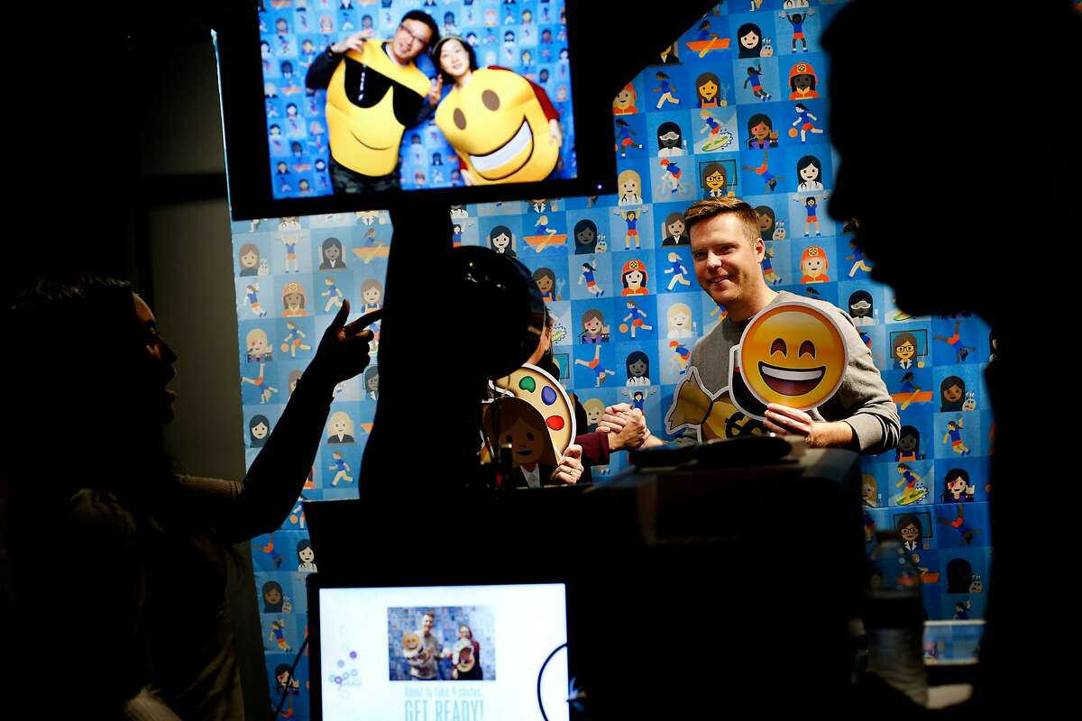From left: Naomi Wardell takes a photo of Daniel Tate, who is holding the Smiling Face With Open Mouth and Smiling Eyes emoji at a photobooth, during the first-ever Emojicon, at the Westfield San Francisco Centre, on Saturday, Nov. 5, 2016 in San Francisco, Calif.