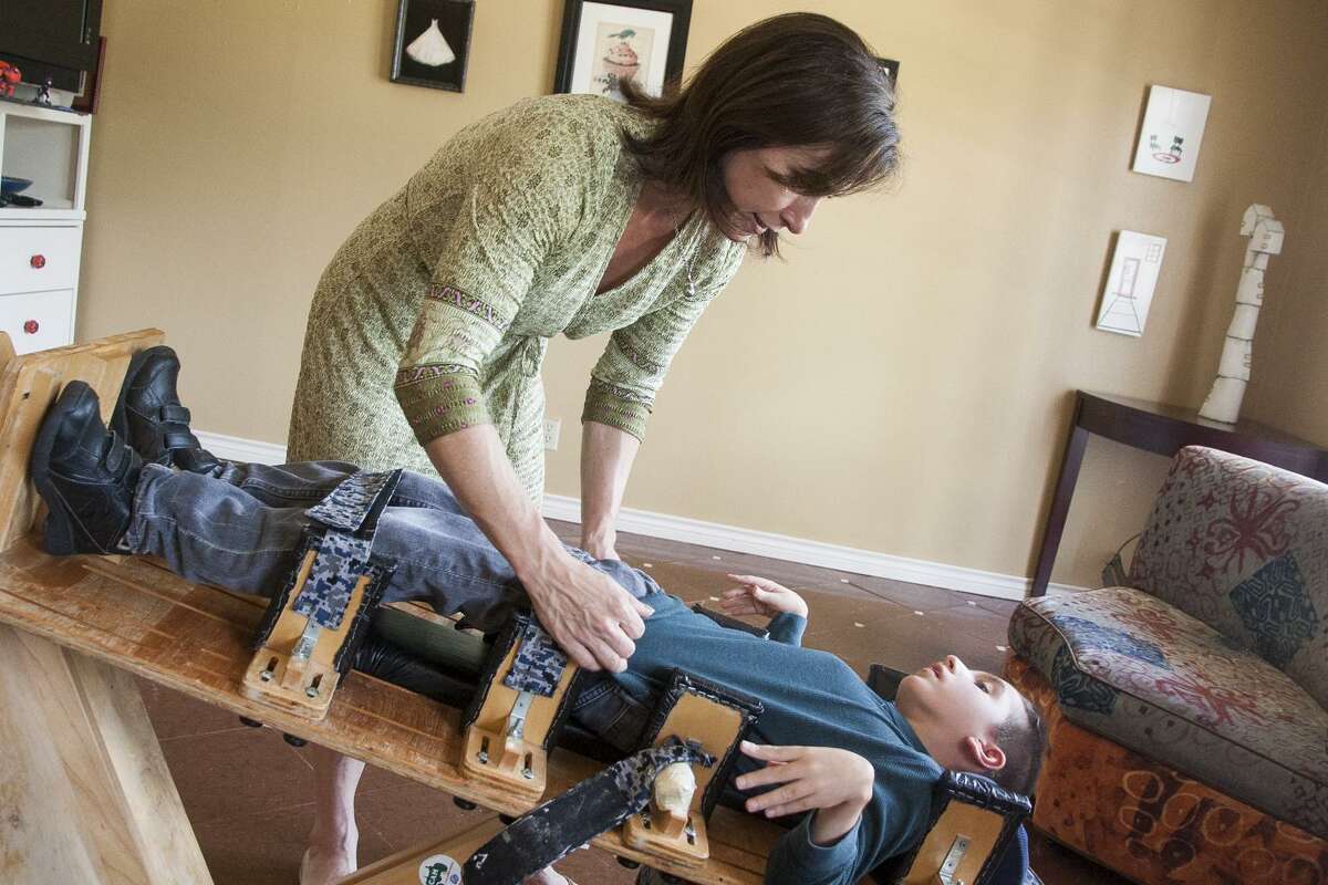 Liz Tullis adjusts and straps her son Conrad, 12, into his upright chair to be fed in April 2015. Many parents of children with anoxic brain injury are advised by doctors to withdraw care or institutionalize the child. A new study suggests these children are more aware than once thought.