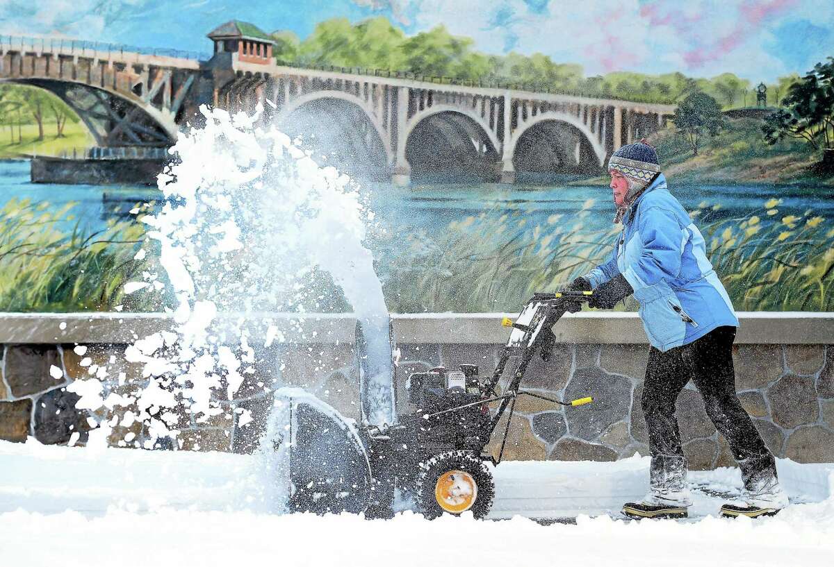 (Arnold Gold-New Haven Register) Nanci Micha clears the snow from the parking lot of the Bridge House Restaurant in Milford on 1/27/2015. Behind her is a mural of the Washington Bridge connecting Stratford with Milford over the Housatonic River.
