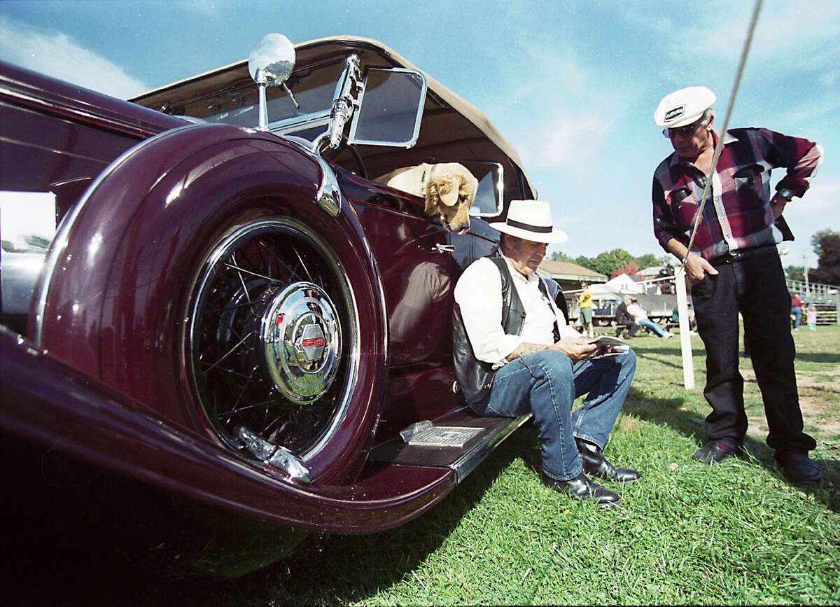 Vin Cahill of Middlefield, sitting on his 1930 Pierce-Arrow Model B, looks at photographs of antique cars with Herb Caso of Cromwell, as his dog, Sam, looks over his shoulder. They are at the Big Antique Car Show and Flea Market at Pat Kidney Field in Middletown.......photo by Irena Pastorello......100100.irenaphoto