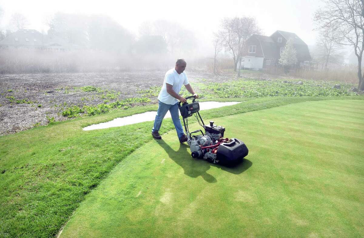 Assistant Course Supervisor Trevor Hill mows the elevated green #2 at the Madison Country Club golf course in Madison on 5/11/2015. In the background is marsh than formerly inundated the green with salt water. Photo by Arnold Gold/New Haven Register agold@newhavenregister.com