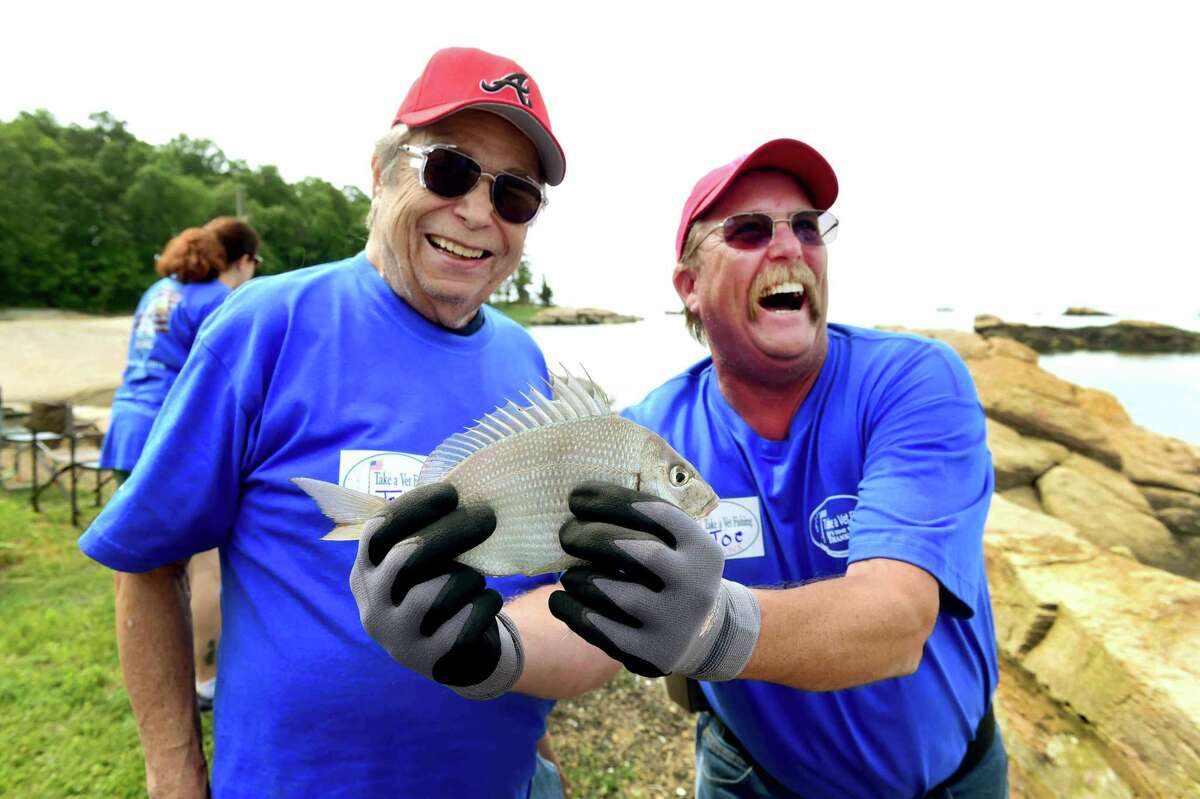 (Peter Hvizdak - New Haven Register) Jon Staski, left, A. U.S. Navy Vietnam War veteran, left, shows off his catch with volunteer Joe Aronson of Middlebury during the First Congregational Church of Branford 10th annual Take-A-Vet Fishing event at Killiam's Point in Branford Thursday morning, June 23, 2016 with Veterans from the West Haven VA Blind Center.