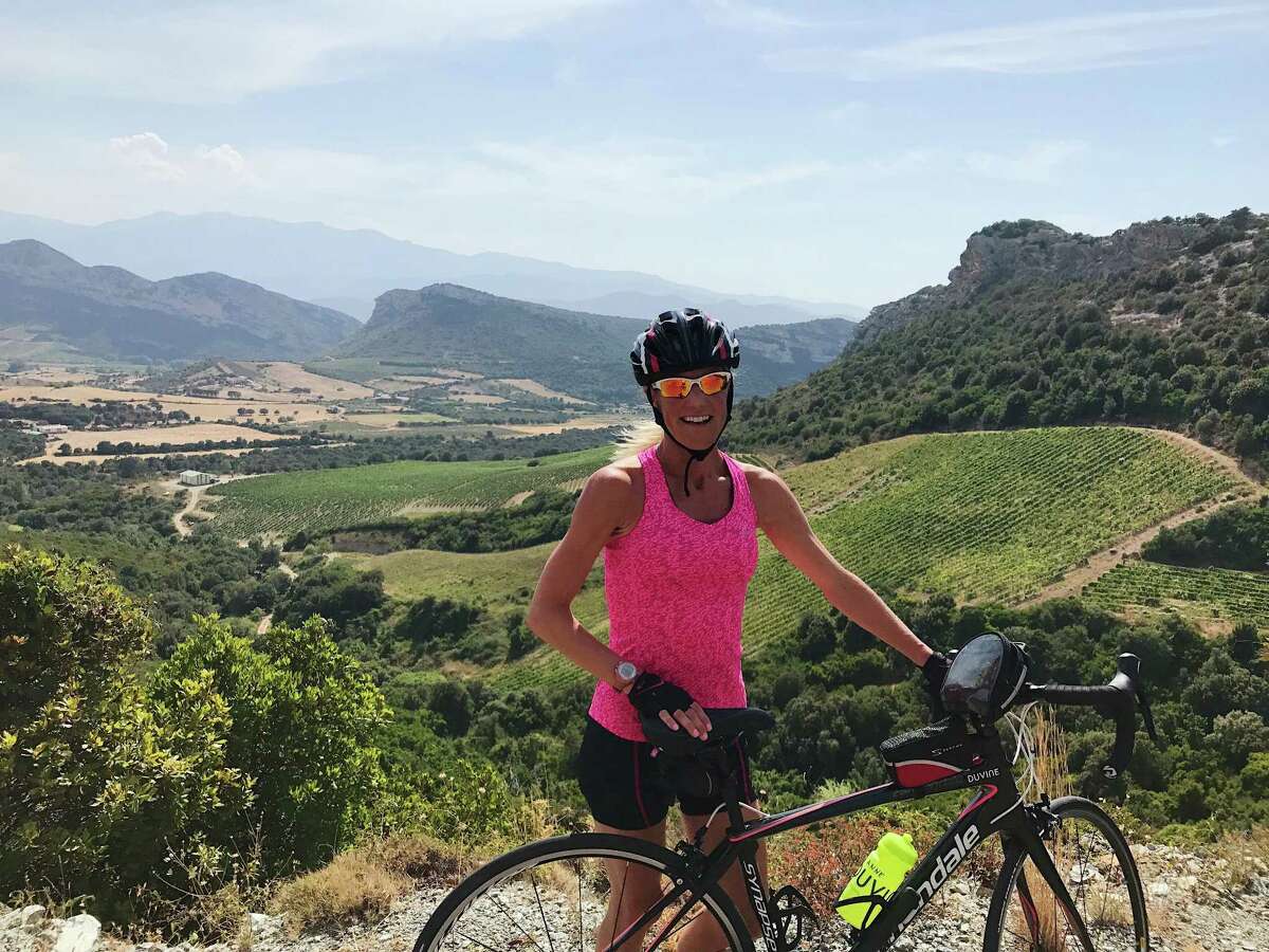 Anne Waldron poses in front of the landscape of Corsica, where she trained to for the Pan-Mass Challenge, an 84 mile bike ride to benefit the Dana Farber Cancer Institute.