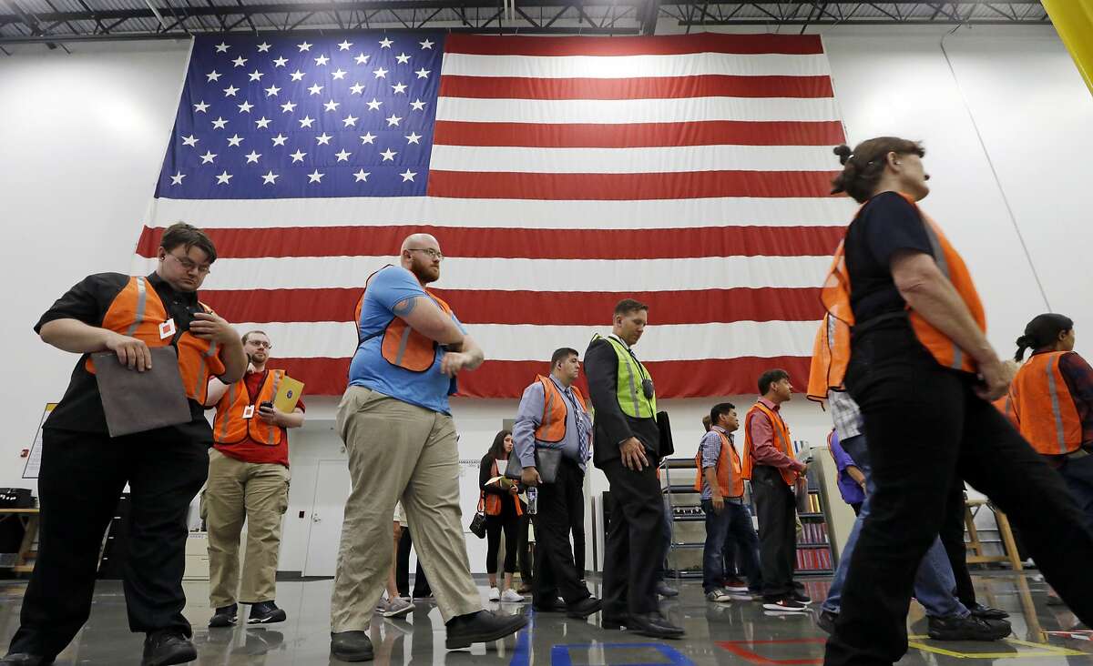 The first group of applicants walks past a giant American flag as they begin a site tour during a job fair, Wednesday, Aug. 2, 2017, at an Amazon fulfillment center, in Kent, Wash. Amazon plans to make thousands of job offers on the spot at nearly a dozen U.S. warehouses during the recruiting event. (AP Photo/Elaine Thompson)