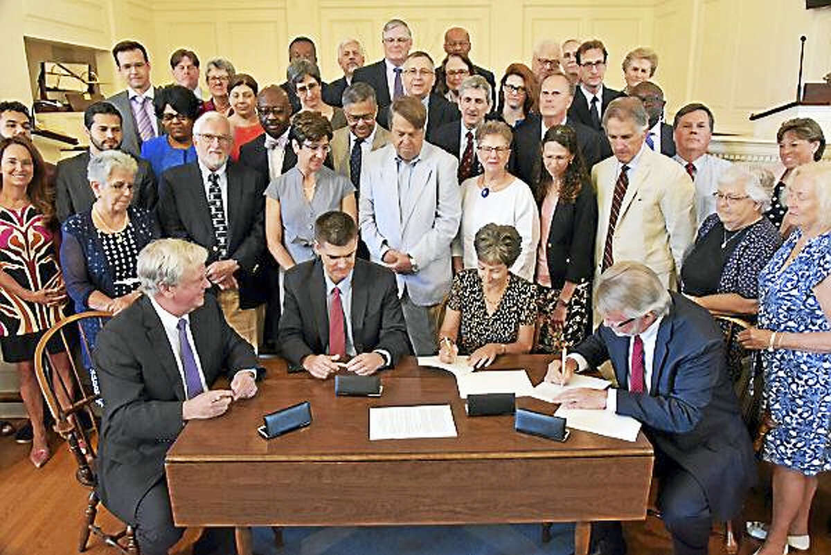 The Rev. Martin B. Copenhaver, president of Andover Newton Theological School, seated at left, and Yale Divinity School Dean Gregory E. Sterling, right, sign a formal affiliation agreement Thursday at the First Church of Christ, Congregational, in Glastonbury.