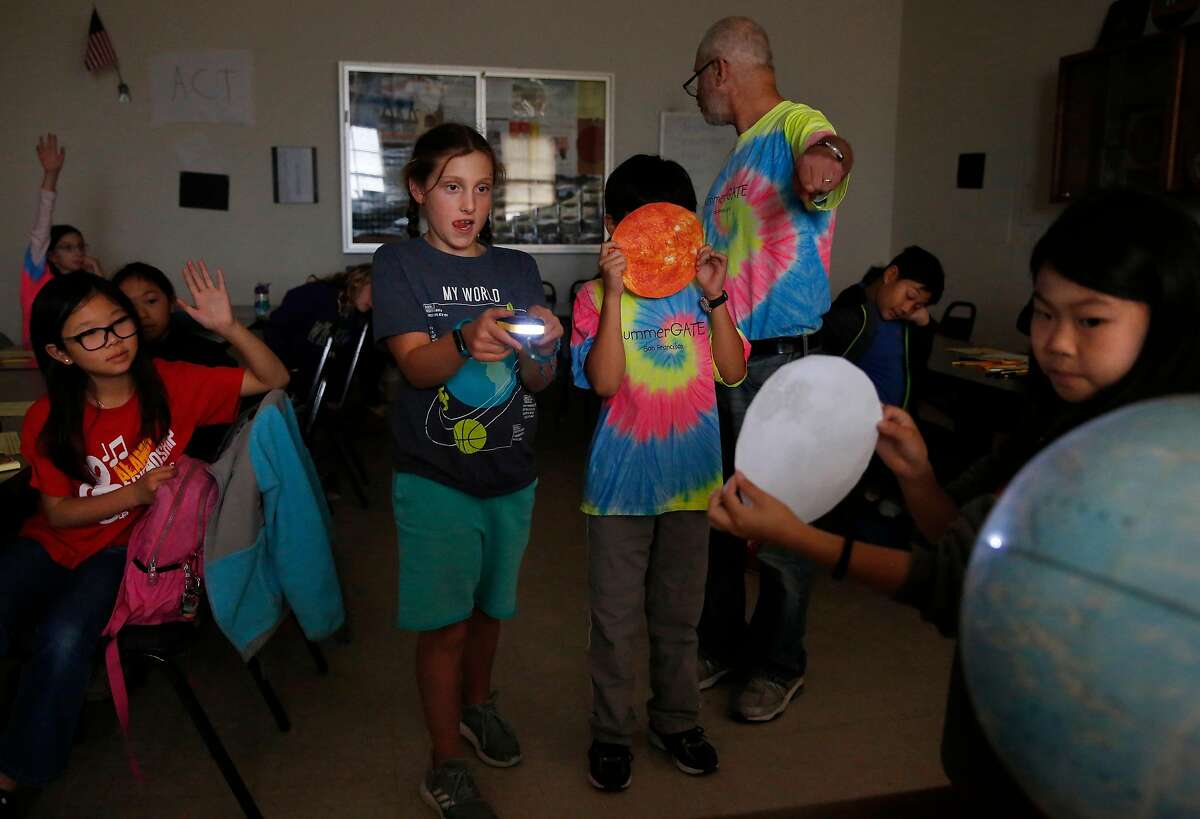 From left, Stephanie Li, 10, watches with other students as Raya Gottsfeld, 10, holds a flashlight simulating the sun's rays for Christopher Gee, 11, as he holds a picture of the sun while Saya Tarm, 9, holds a picture of the moon and moves it across the globe representing the earth, thereby simulating what happens to cause a solar eclipse as their teacher Alex Hertz explains it during a SummerGATE class at St. Anne's campus August 3, 2017 in San Francisco, Calif.