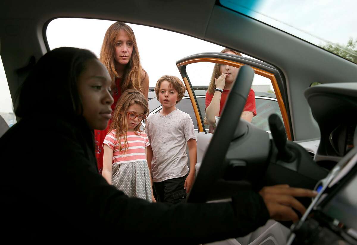Sales associate Devani Knox (left) explains functions of the Bolt EV all-electric car to Dana Nachman and her children Sidney, 7, Charlie, 10, and Annie, 11, after a test drive at a Chevrolet dealership in Fremont, Calif. on Friday, Aug. 4, 2017. Proposed state legislation may provide instant rebates to boost sales of plug-in vehicles.
