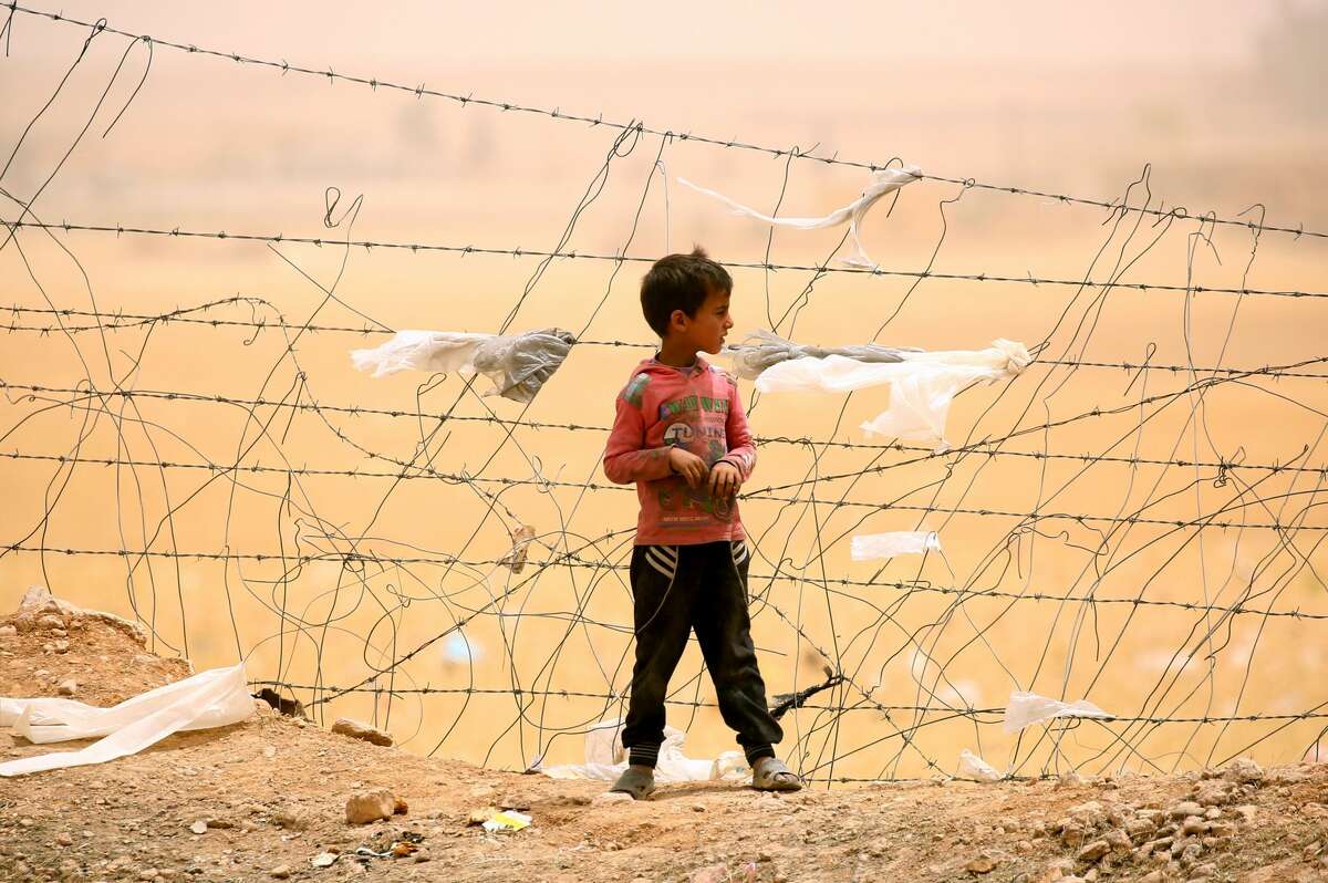 A displaced Syrian boy who fled the Islamic State group stronghold of Raqa stands near a fence during a sandstorm at a temporary camp in a northern Syrian village.
