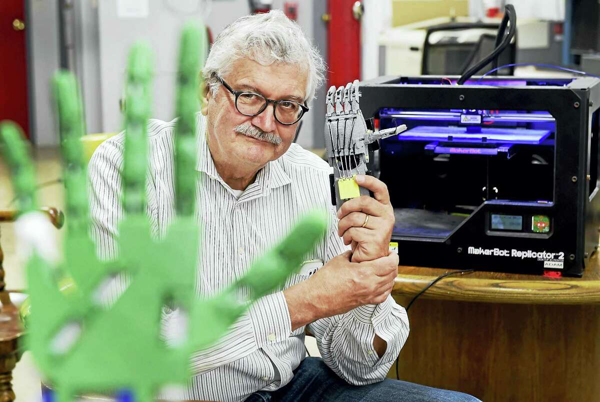 (Peter Hvizdak - New Haven Register)New Haven, Connecticut: May 7, 2017. Using a 3D printer, Bruce O'Donnell, 66, of Cheshire, Connecticut is framed by a robotic hand and arm prosthetic prototype, left, and holds a functional mechanical prosthetic, made at MakeHaven in New Haven.