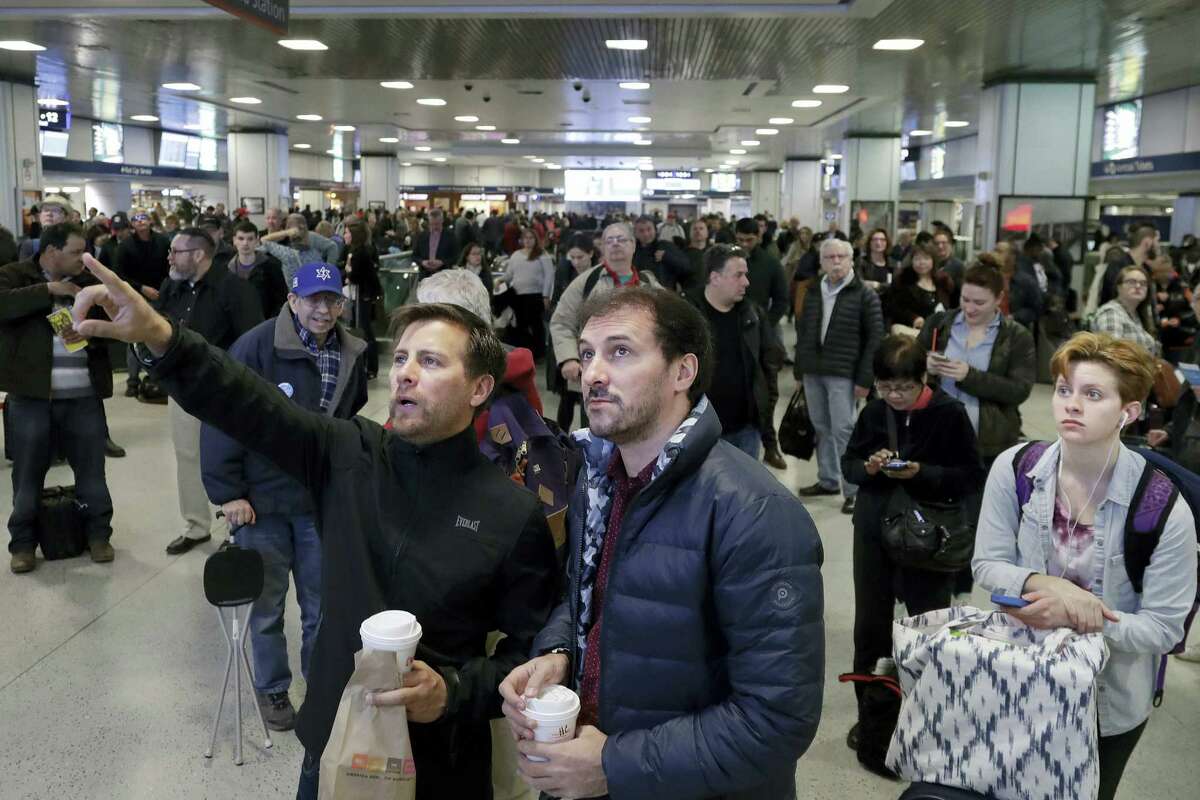FILE - In this April 3, 2017 file photo, waiting commuters and passengers in New York's Penn Station look up to a train schedule board after delays were created when a train derailed earlier in the day. New Jersey Transit said one of its trains derailed while pulling into the station at a slow speed. The derailment comes a week and a half after an Amtrak train partially derailed as it pulled out of Penn Station. (AP Photo/Mark Lennihan, File)