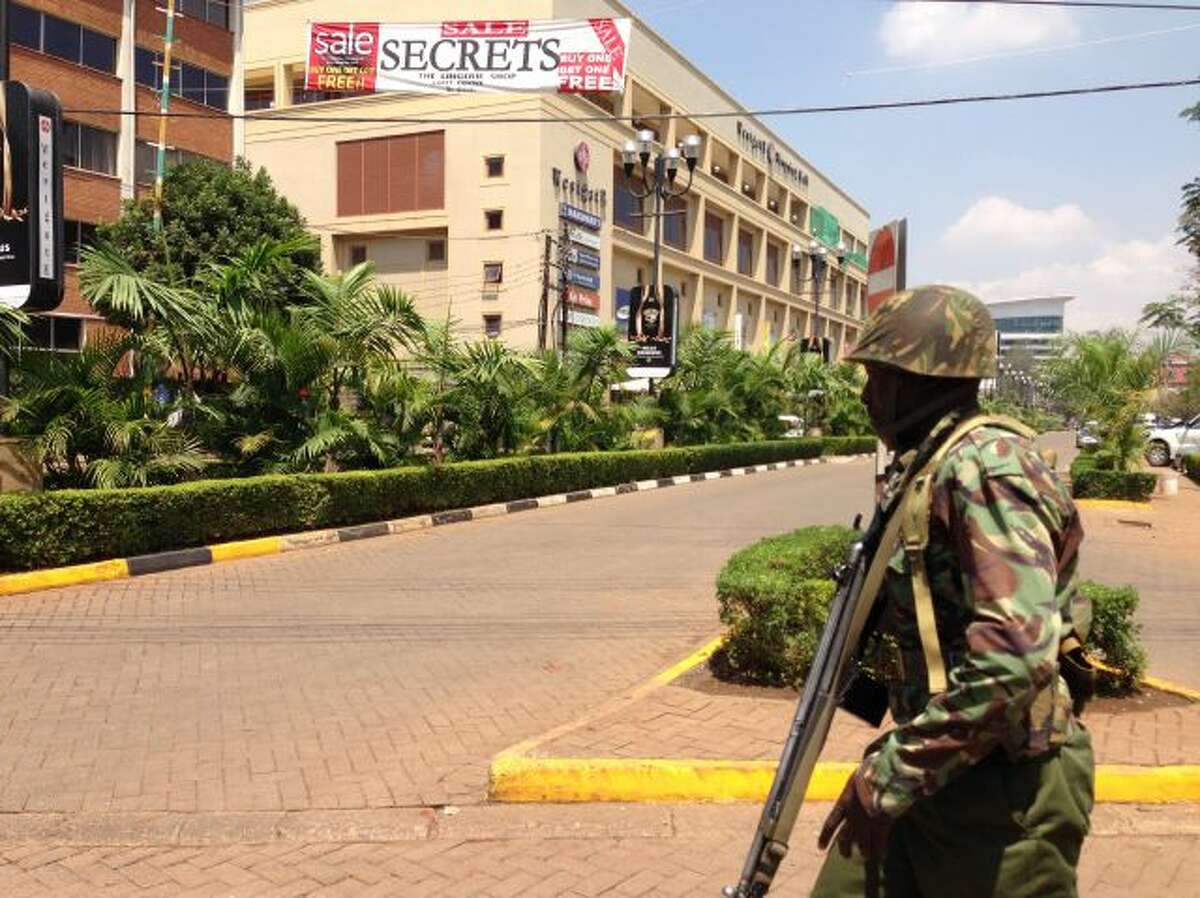 A soldier moves to take up a position outside an upscale shopping mall, seen background, in Nairobi, Kenya Saturday Sept. 21 2013, where shooting erupted when armed men attempted to rob a shop, according to police. Witnesses say a half dozen grenades also went off along with lobbies of gunfire that started at midday. (AP Photo/ Jason Straziuso)