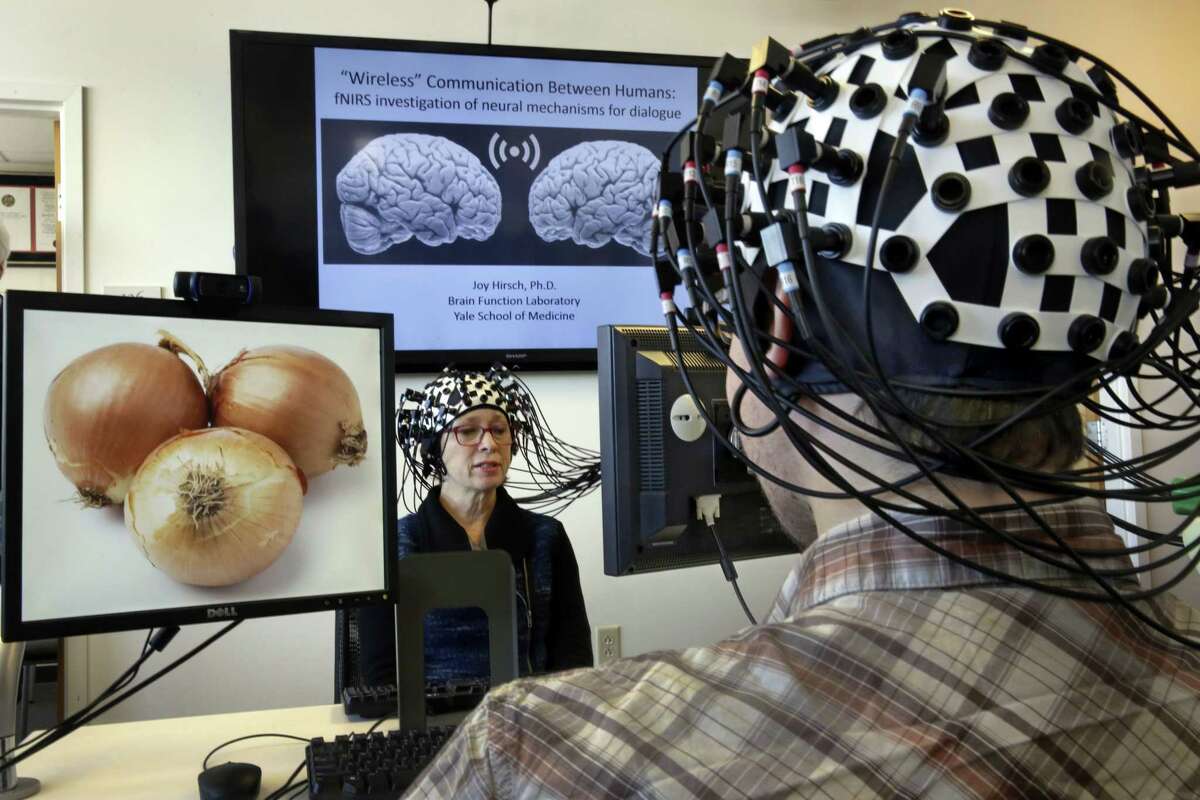 ADVANCE FOR USE MONDAY, JUNE 22, 2014 AND THEREAFTER - Shaw Bronner, left, and Shaul Yahil, two researchers at the Yale Brain Function Lab, describe images on their computer screens to each other while their brain activity is mapped during a demonstration of the technology in New Haven, Conn. on Friday, March 13, 2015. At one end of each of the 64 fiber optic cables in each headpiece, weak laser beams saw about an inch into their brains to detect blood flow. (AP Photo/Richard Drew)