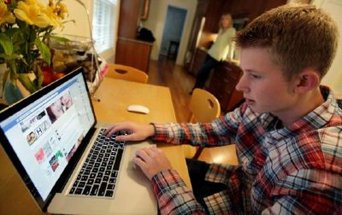 In this Oct. 24, 2013 photo, Mark Risinger, 16, checks his Facebook page on his computer as his mother, Amy Risinger, looks on at their home in Glenview, Ill. The recommendations are bound to prompt eye-rolling and LOLs from many teens, but an influential pediatrician's group says unrestricted media use has been linked with violence, cyber-bullying, school woes, obesity, lack of sleep and a host of other problems.
