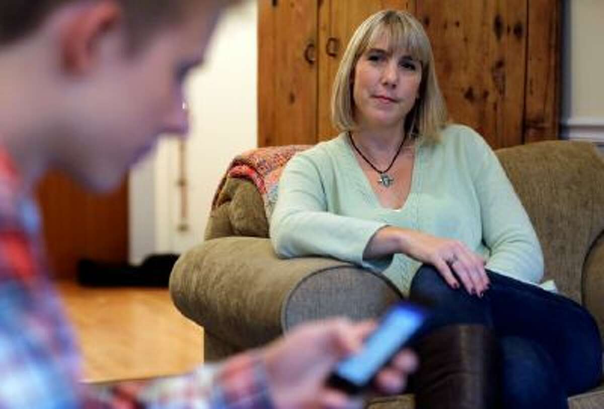In this Oct. 24, 2013 photo, Amy Risinger, right, watches her son Mark Risinger, 16, at their home in Glenview, Ill. Mark Risinger is allowed to use his smartphone and laptop in his room, and says he spends about four hours daily on the Internet doing homework, using Facebook and YouTube and watching movies.