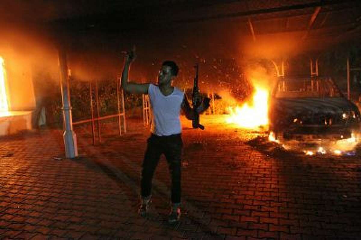 An armed man waves his rifle as buildings and cars are engulfed in flames after being set on fire Sept. 11, 2012, inside the U.S. consulate compound in Benghazi, Libya.