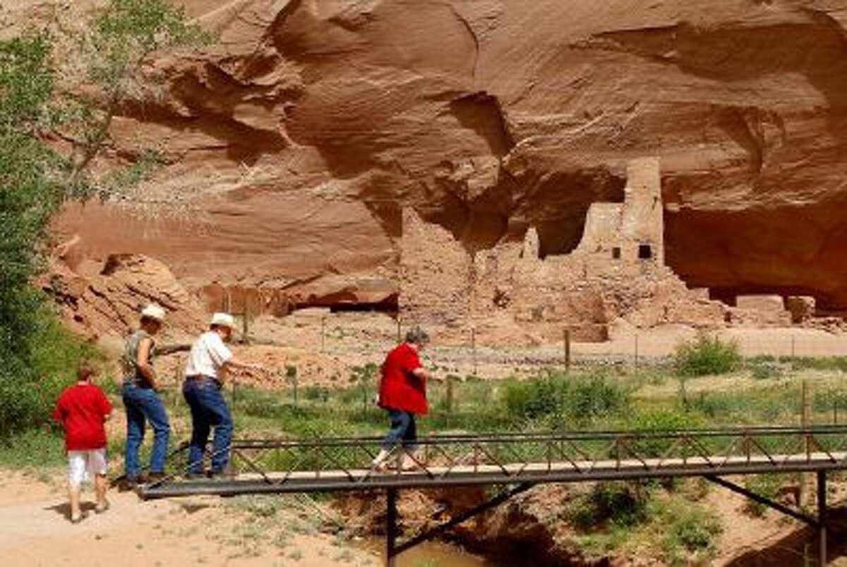 Tourists walk along a bridge in front of ruins inside Canyon de Chelly National Monument, near Chinle, Ariz.