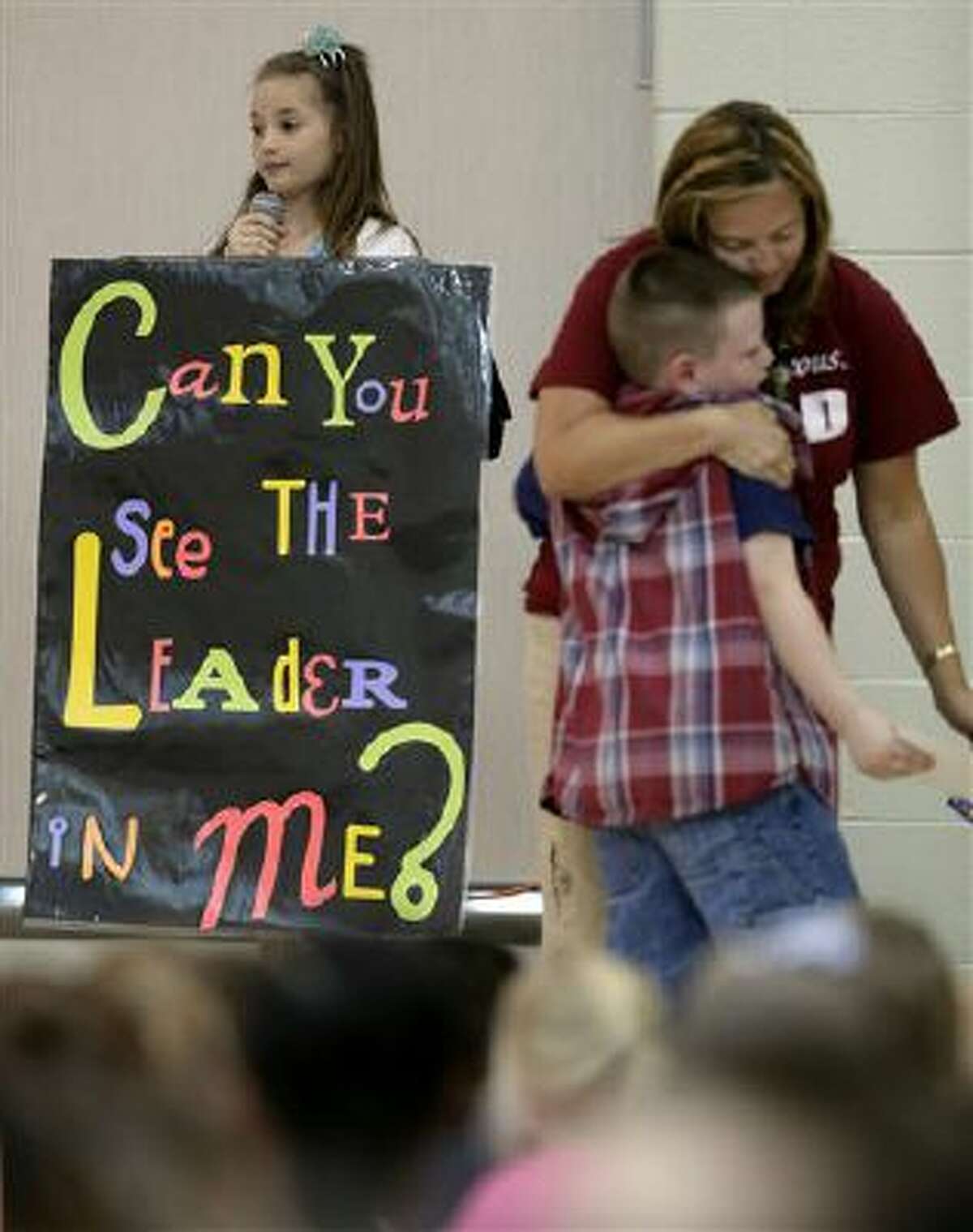 In this photo taken Friday, Sept. 6, 2013, third-grader Jonathan Kent gets a hug from his teacher Mandy Brown after getting an award during a monthly leadership assembly presided over by fourth-grader Anita Bedworth at Indian Trails Elementary school in Independence, Mo.