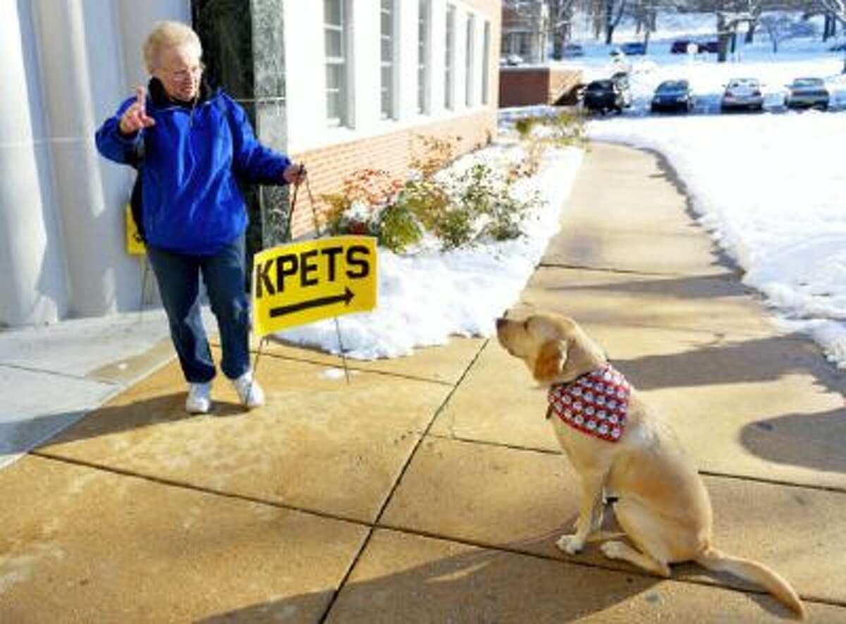Keystone Pet-Enhanced Therapy Service handler Harriet Hombach instructs her Labrador retriever Corky to sit as she places signs to direct York College students to a room inside the student union where they could play with therapy dogs on Wednesday in York, Penn.