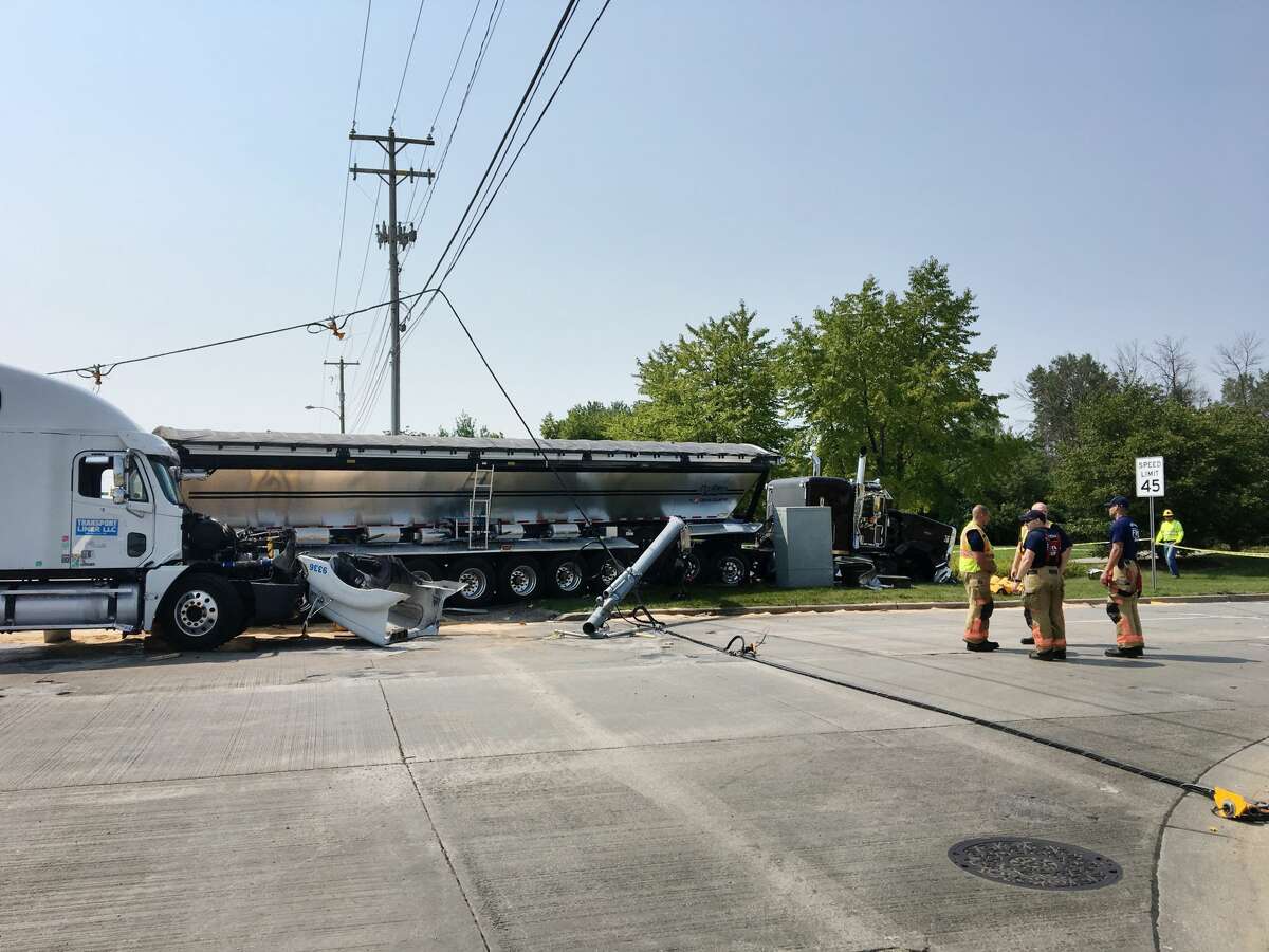 Midland firefighters stand near two tractor-trailers after they collided while driving northbound on Washington Street, causing one to knock down a traffic light, at the intersection of Washington and Patrick on Tuesday.