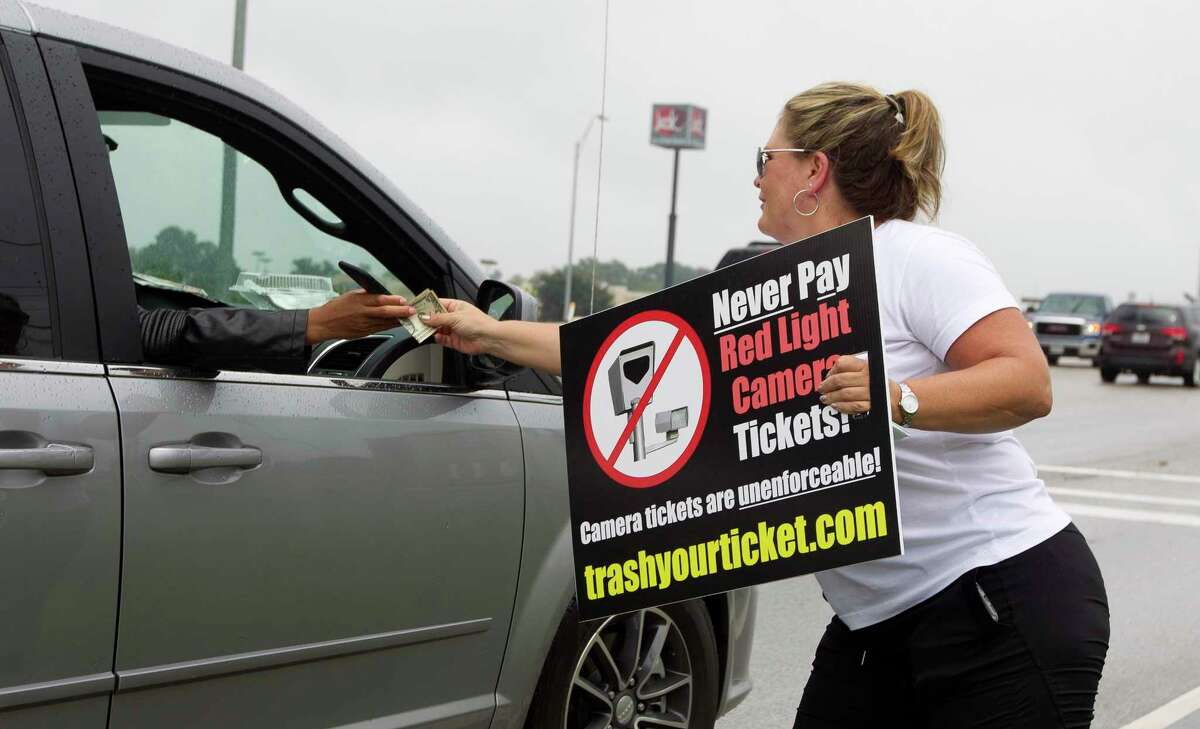 Kelli Cook receives money from a passing motorist as she and others protest red light cameras on the corner of FM 1097 and I-45, Tuesday, Aug. 8, 2017, in Willis.