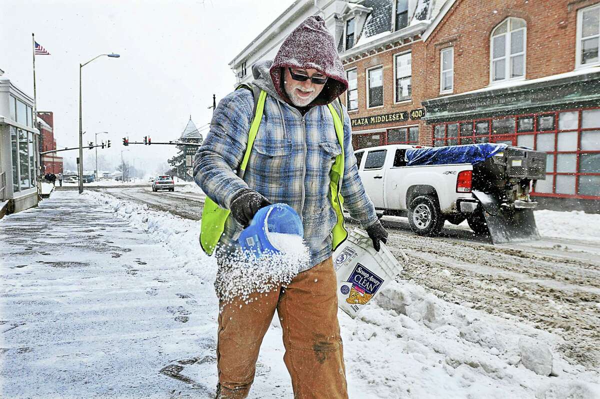 A man sprinkles salt on the sidewalk on College Street at Citizen Bank in Middletown in this archive photograph. Meteorologists are predicting the entire state will be blanketed by up to 10 inches of snow following a storm expected to begin late Wednesday and stretch into Thursday.