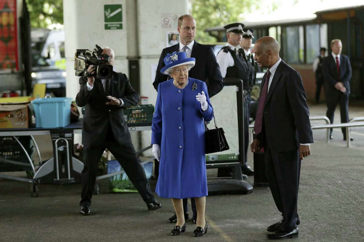 Britain’s Queen Elizabeth II and William the Duke of Cambridge, centre rear, look towards Grenfell Tower as they visit the the Westway sports centre which is providing temporary shelter for those who have been made homeless in the fire disaster in London, Friday, June 16, 2017. Relatives of those missing after a high-rise tower blaze in London are searching frantically for their loved ones, as the police commander in charge of the investigation says he hopes the death toll will not rise to three figures.