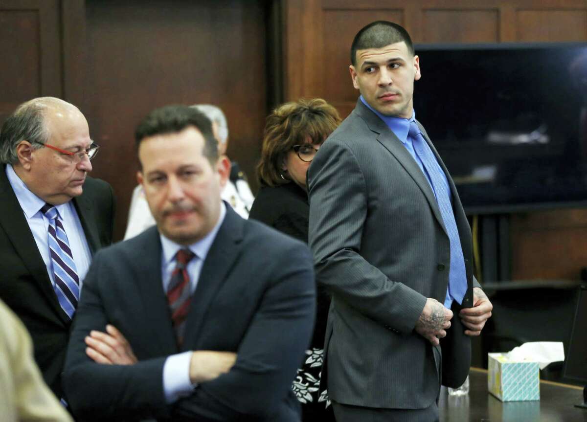 Defendant Aaron Hernandez, right, stands and looks as his attorneys confer during his double murder trial at Suffolk Superior Court, Tuesday, April 11, 2017, in Boston. Hernandez is on trial for the July 2012 killings of Daniel de Abreu and Safiro Furtado who he encountered in a Boston nightclub. The former New England Patriots NFL player is already serving a life sentence in the 2013 killing of semi-professional football player Odin Lloyd.