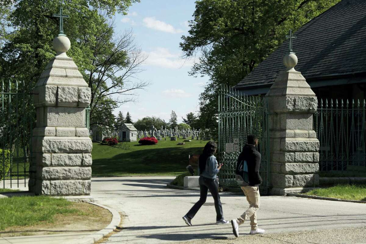 People walk past a gate to Holy Cross Cemetery, Wednesday, May 3, 2017, in Yeadon, Pa. The body of 19th century serial killer Dr. H. H. Holmes is being exhumed from the cemetery in suburban Philadelphia at the request of his great-grandchildren, who hope identifying his remains will quell centuries-old rumors that he conned his way out of his execution and escaped from prison.