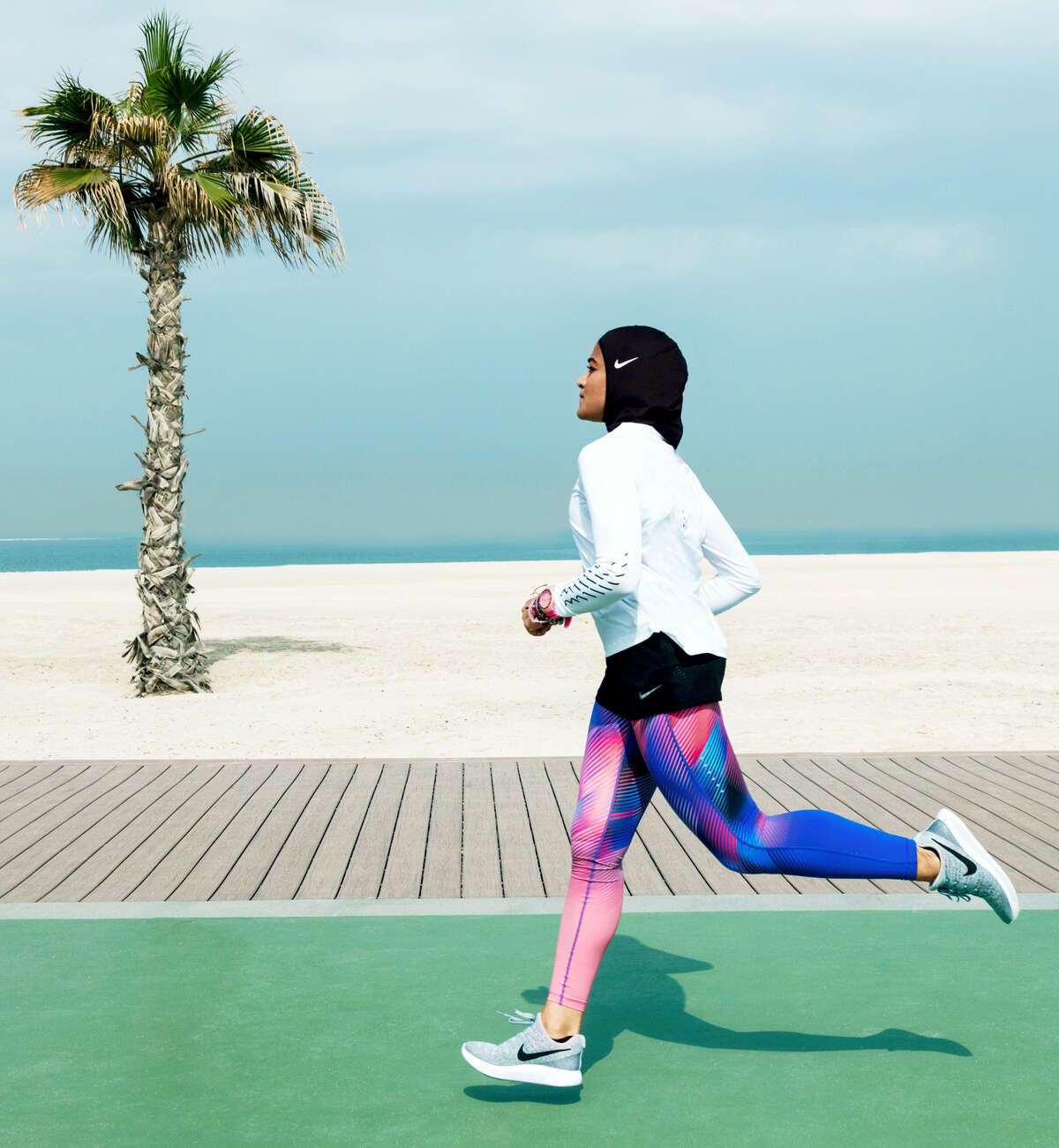 In this undated image provided by Nike, Manal Rostom jogs wearing Nike’s new hijab for Muslim female athletes. The pull-on hijab is made of light, stretchy fabric that includes tiny holes for breathability and an elongated back so it will not come untucked. It will come in three colors: black, vast grey and obsidian. Beaverton-based Nike says the hijab will be available for sale next year.